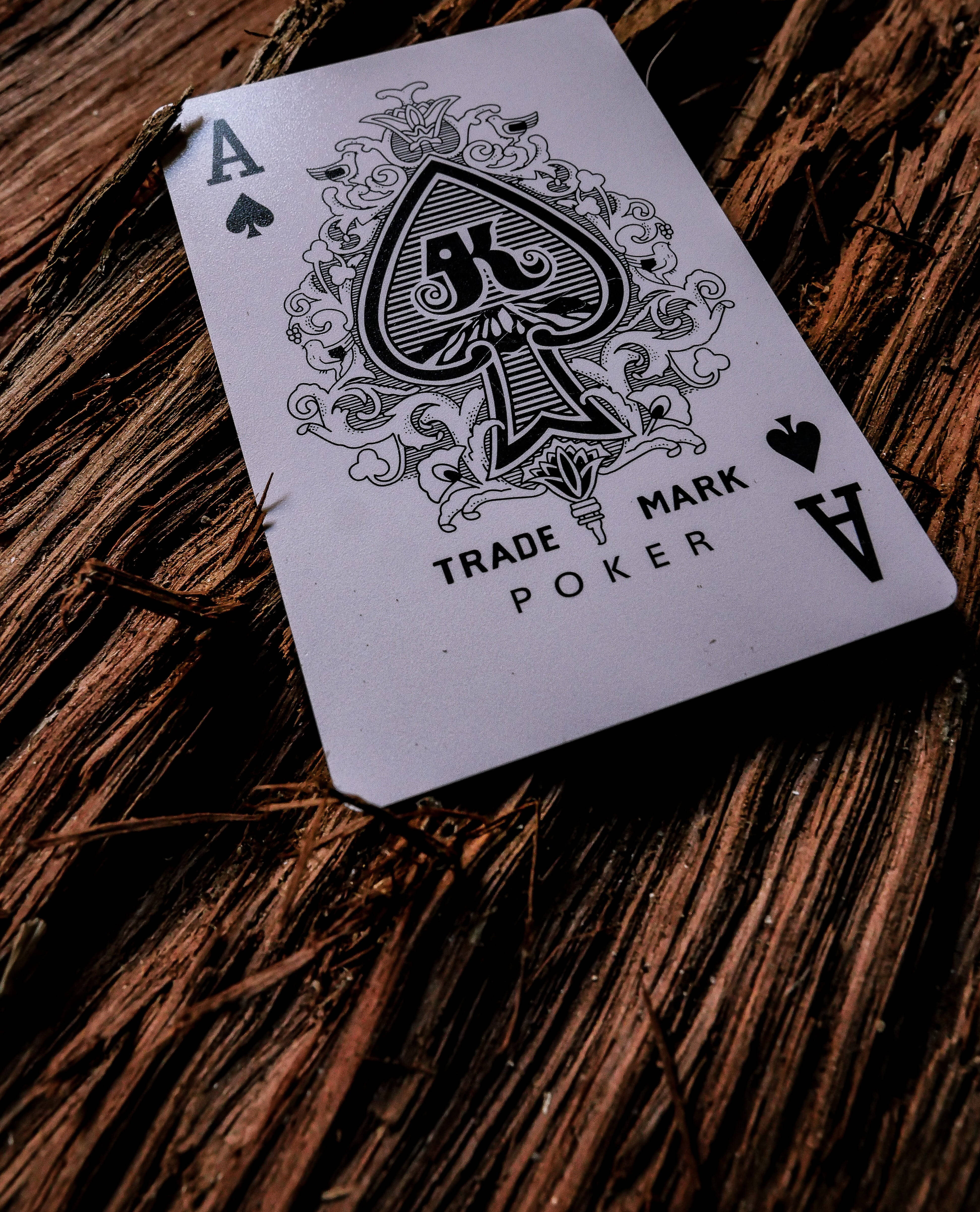 Poker 桌布 壁紙 — 一張裝飾性的黑桃A撲克牌斜放在紋理豐富的棕色木質表面上，帶有戲劇性的燈光效果。