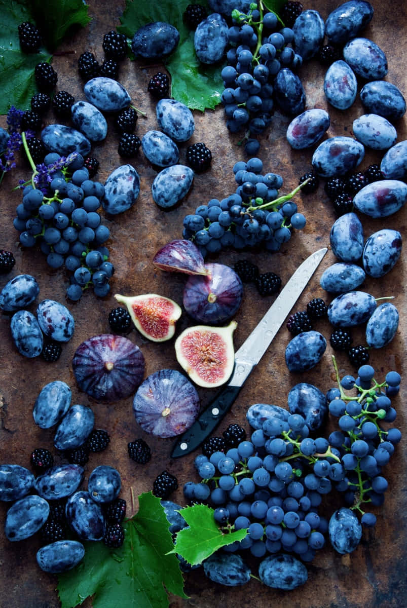 Fruits 桌布 壁紙 — 一張質樸的俯拍照片，展示飽滿的藍色葡萄、無花果和黑莓，搭配一把刀，擺放在經風化的木質表面上。