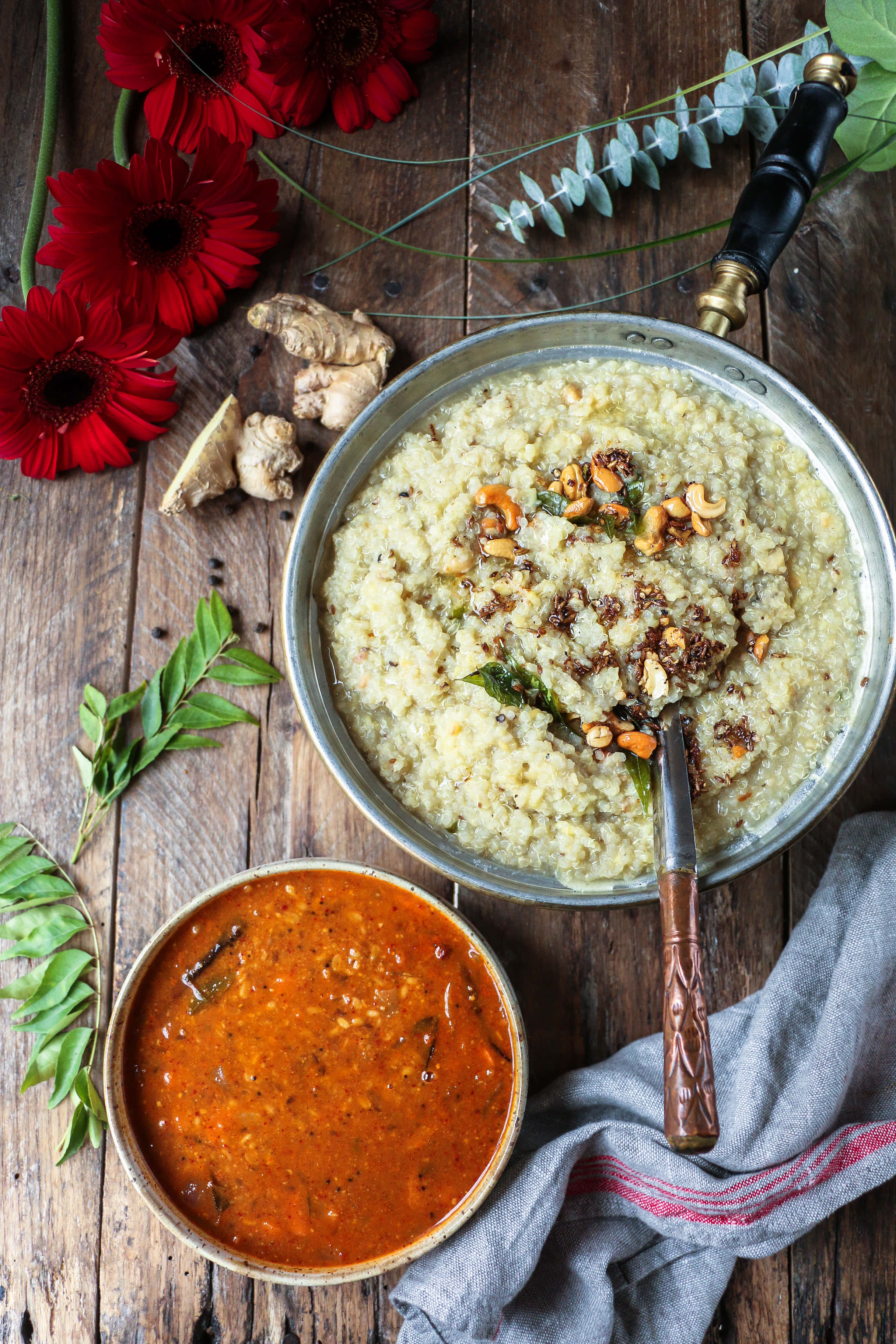 Pongal 桌布 壁紙 — 一張質樸的木桌上，一個金屬碗盛載著奶油米飯，上面放有腰果和咖喱葉，旁邊有一碗紅咖喱醬和新鮮的紅色非洲菊雛菊。