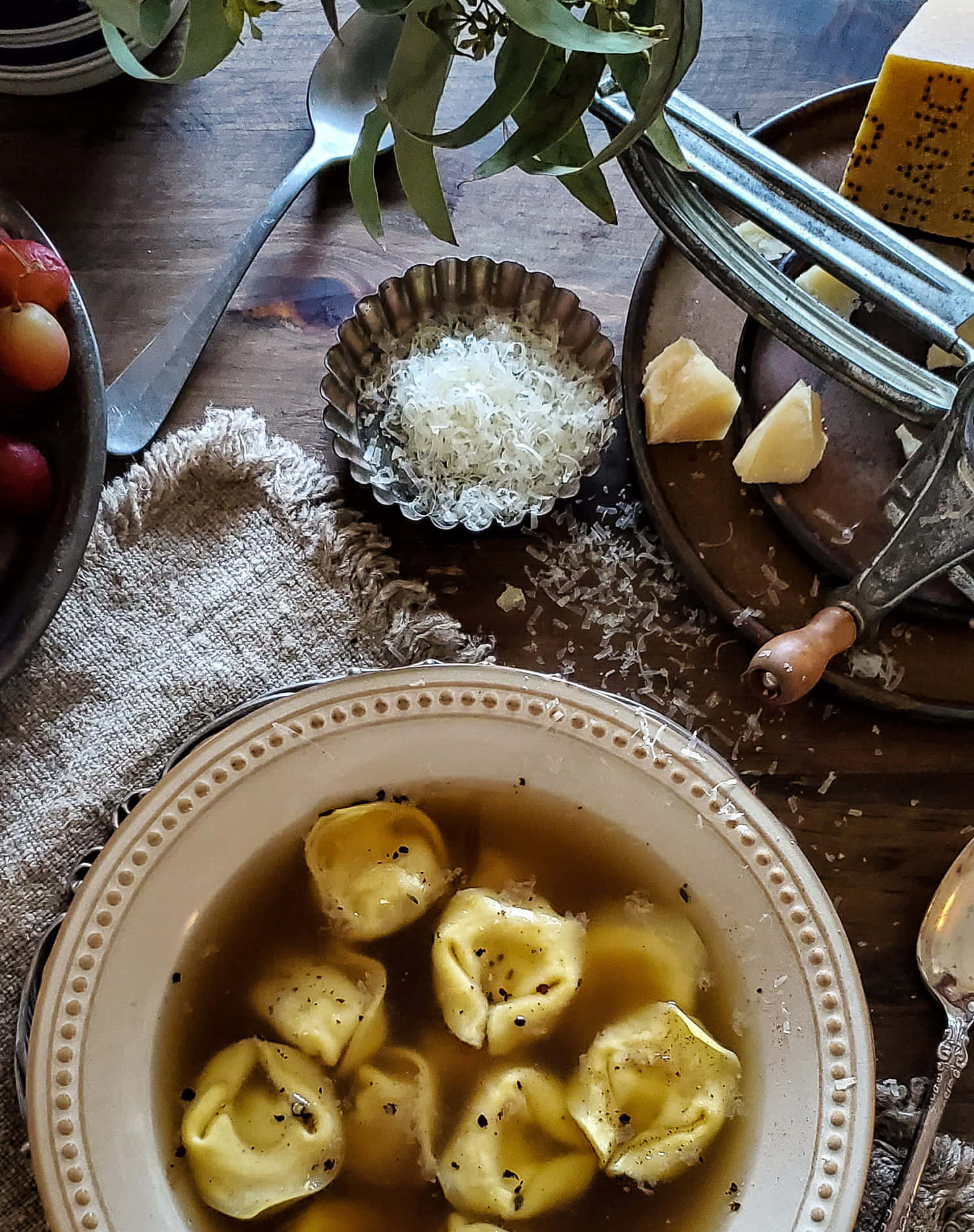Food Photography 桌布 壁紙 — 一張質樸的木桌上，放著一碗放在肉湯中的義大利餃子，上面撒有黑胡椒和磨碎的起司，還有新鮮葡萄和一個起司刨。