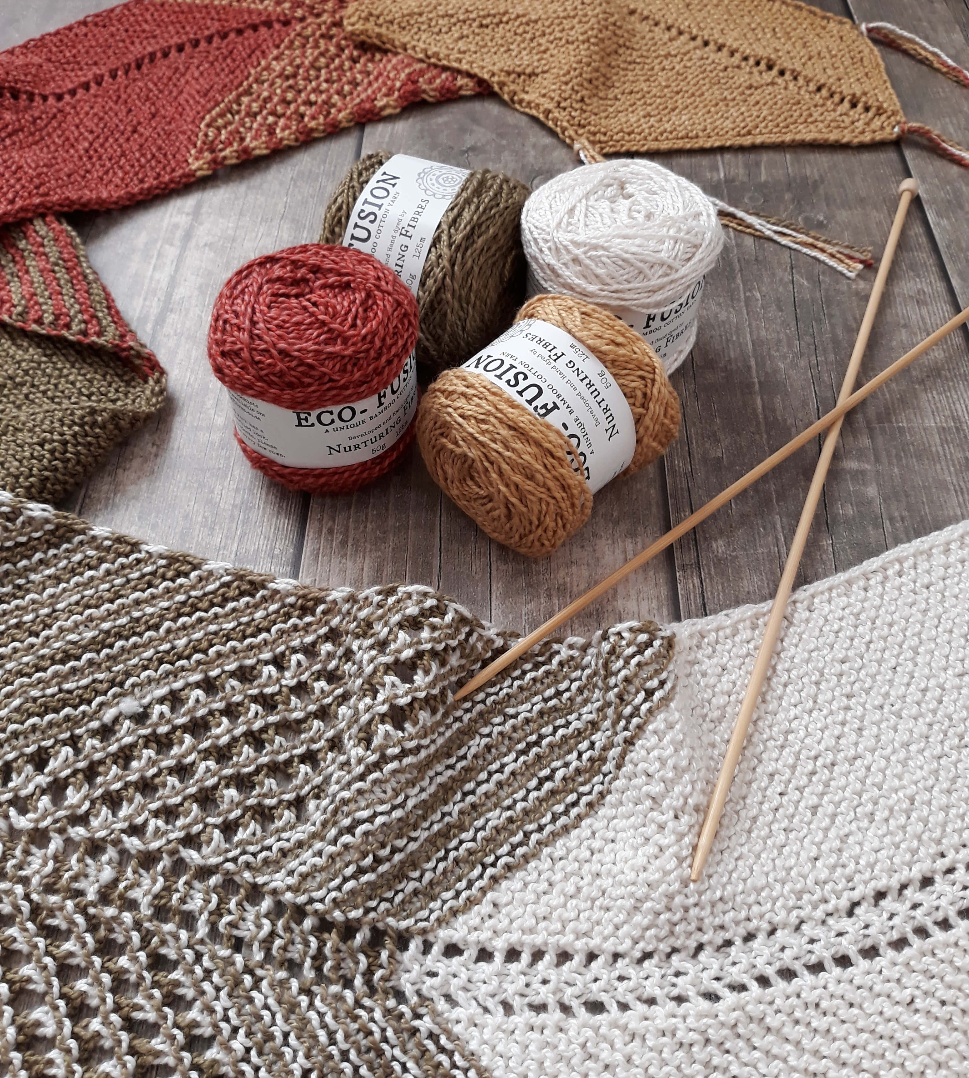 Crocheting 桌布 壁紙 — 一張質樸的木桌上展示著色彩繽紛的毛線球、編織針和部分完成的質感針織布料，色調樸實。