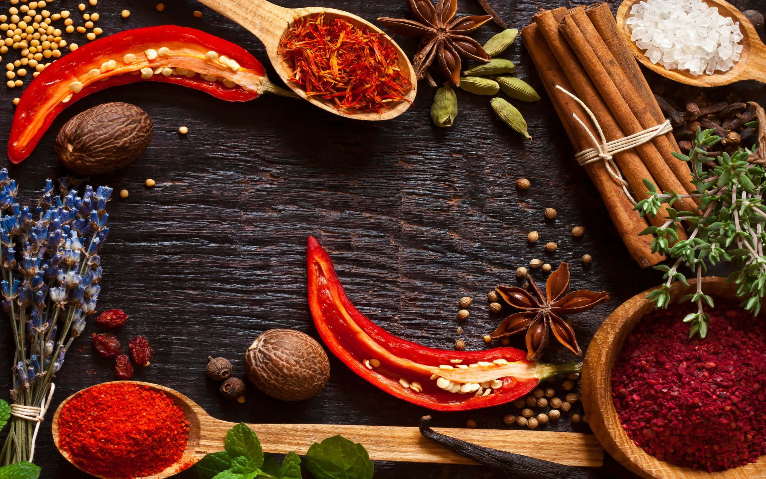 Spice 桌布 壁紙 — 一張質樸的木桌上展示著鮮豔的香料和香草，如紅辣椒、藏紅花、肉桂和八角，排列在勺子和碗中。