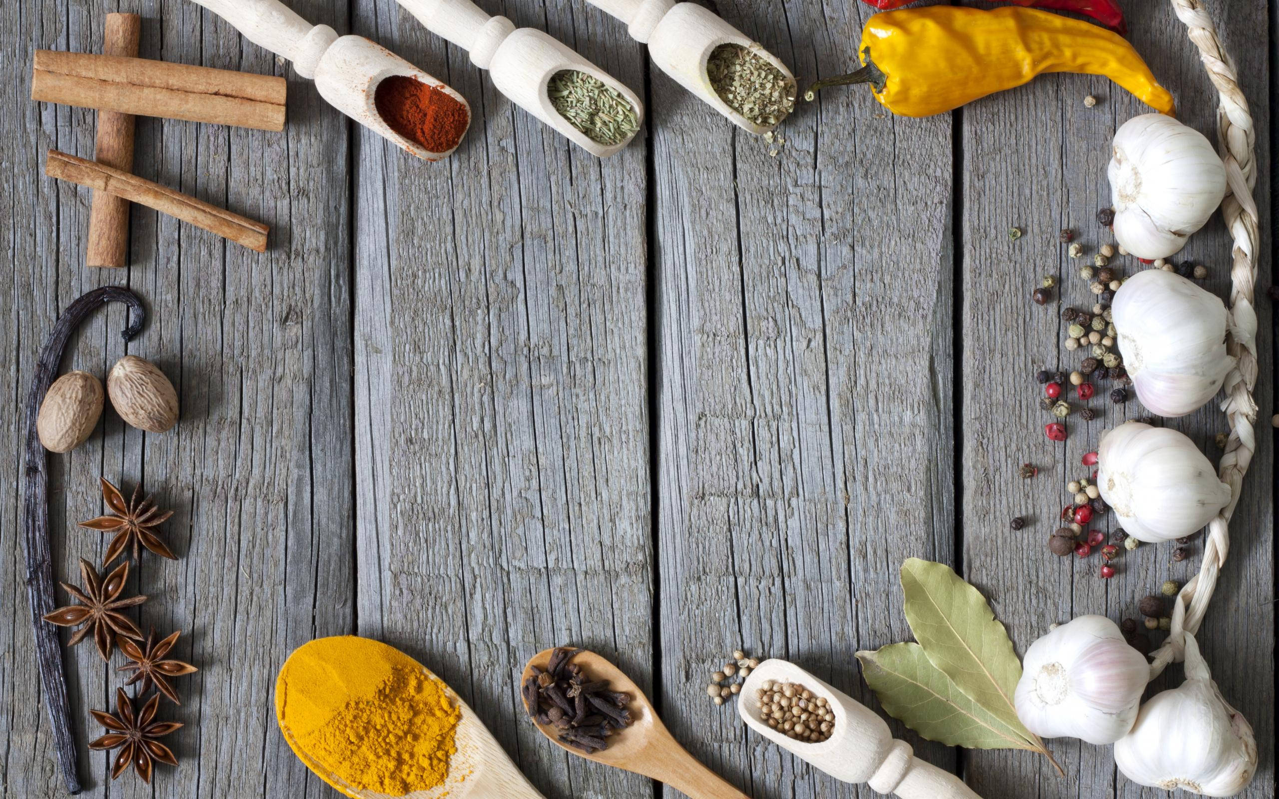 Spice 桌布 壁紙 — 一張質樸的木桌上擺放著各式各樣的香料和香草，以木勺和完整形態呈現，營造出豐富的烹飪場景。