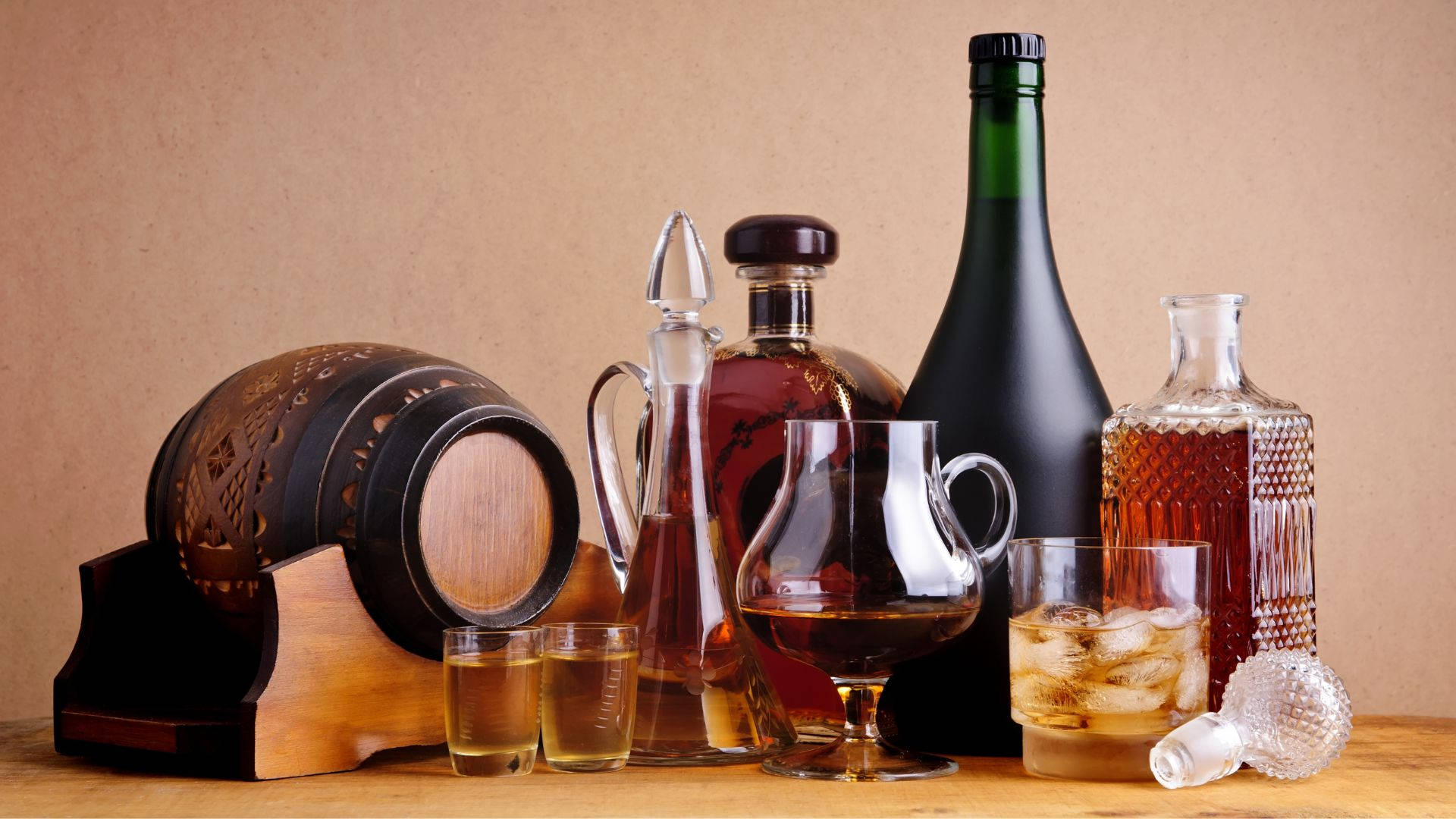alcohol 桌布 壁紙 — 一張質樸的木桌上擺放著各種威士忌酒瓶、酒杯和一個裝飾性木桶，背景是溫暖的米色。