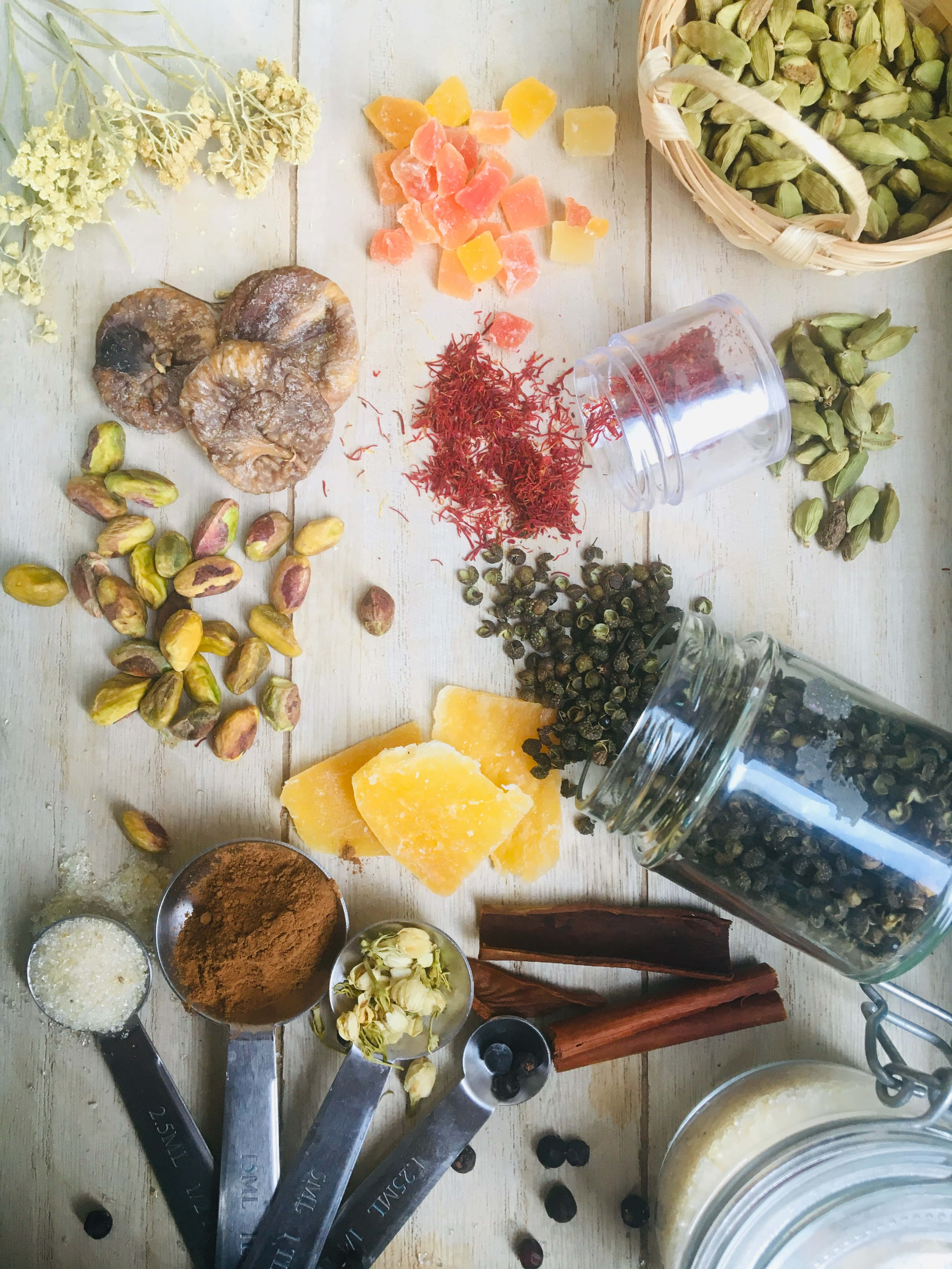 Spices 桌布 壁紙 — 一張質樸的木桌上擺放著各種色彩鮮豔的香料和乾燥食材，包括番紅花、開心果、小荳蔻和肉桂，以平鋪構圖呈現。