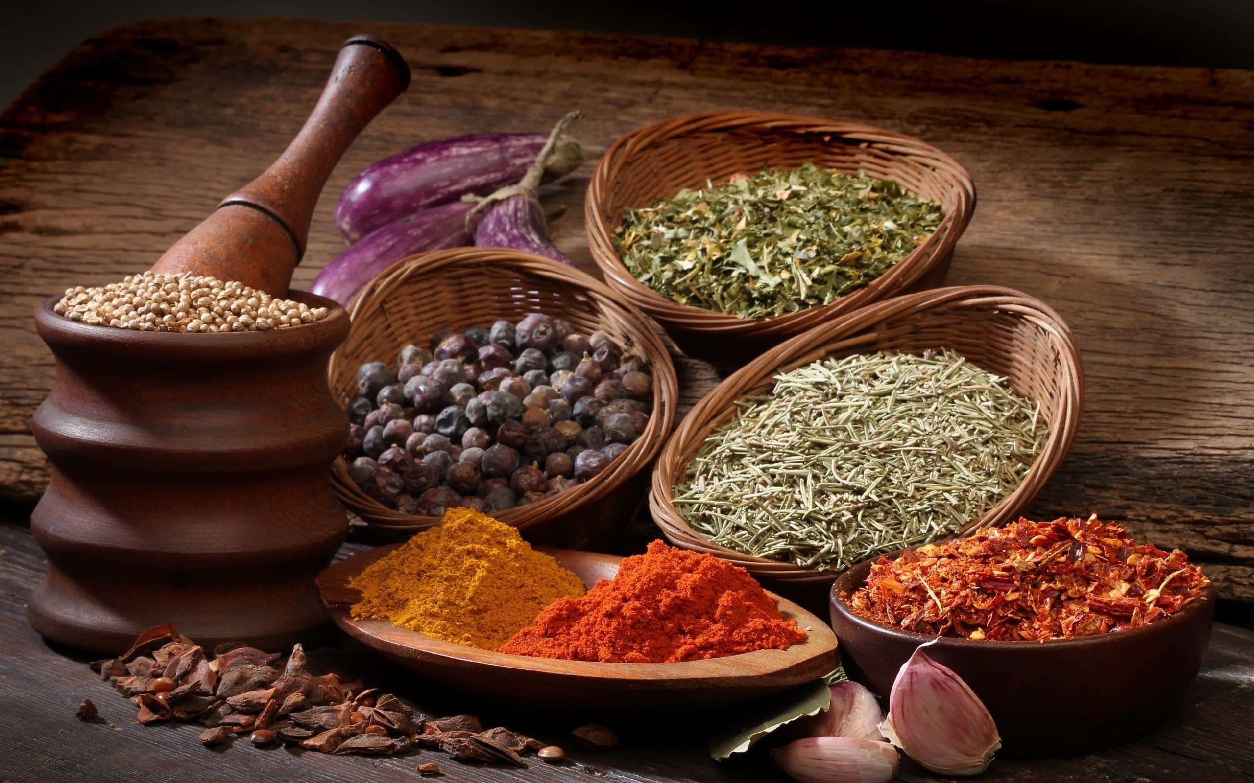 Spices 桌布 壁紙 — 一張質樸的木桌上擺放著編織籃子和碗中的鮮豔香料和香草，旁邊還有大蒜、茄子和研缽。