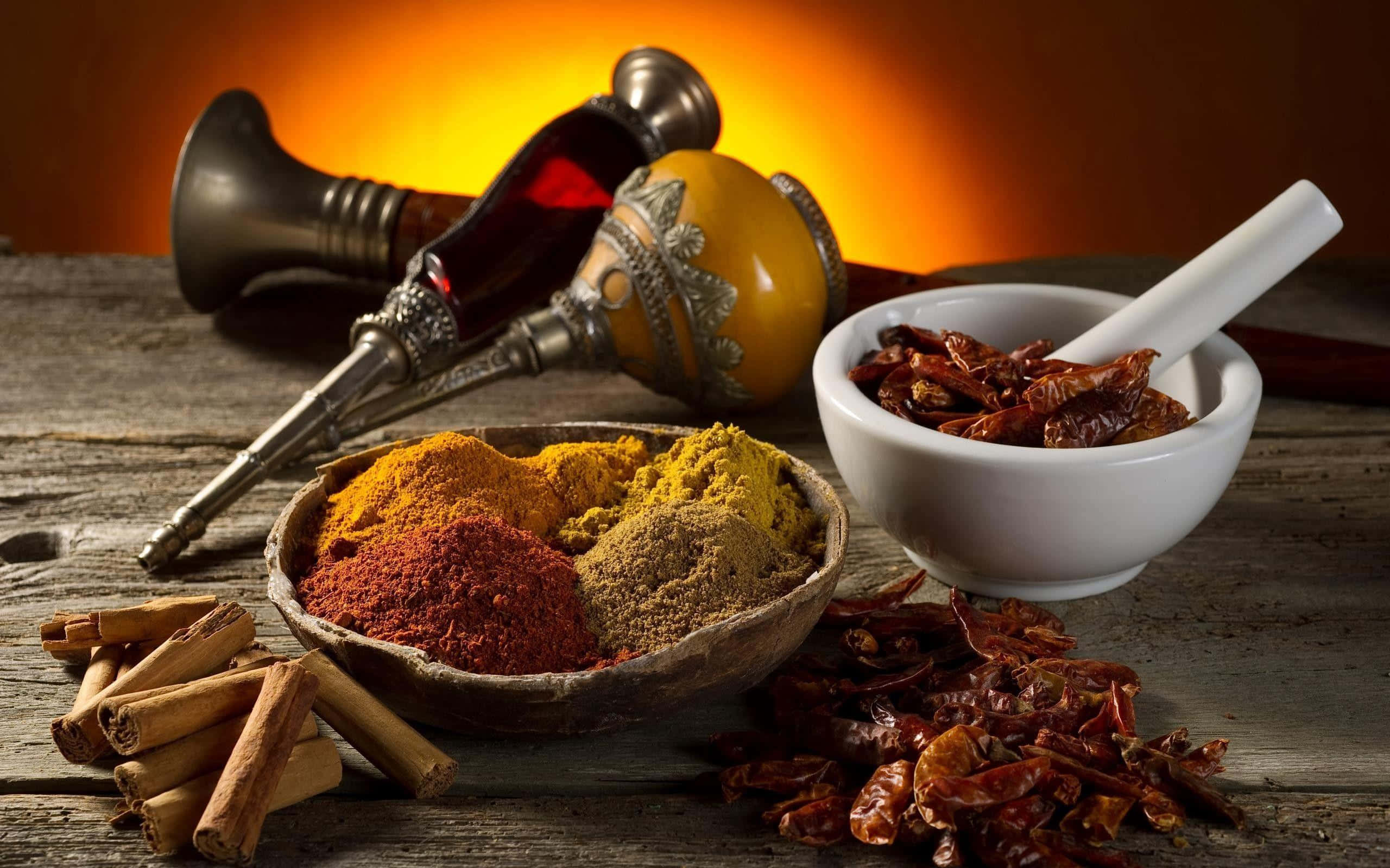 Spices 桌布 壁紙 — 一張質樸的木桌上擺放著色彩鮮豔的香料、肉桂棒、乾辣椒和研缽，背景是溫暖的金色燈光。