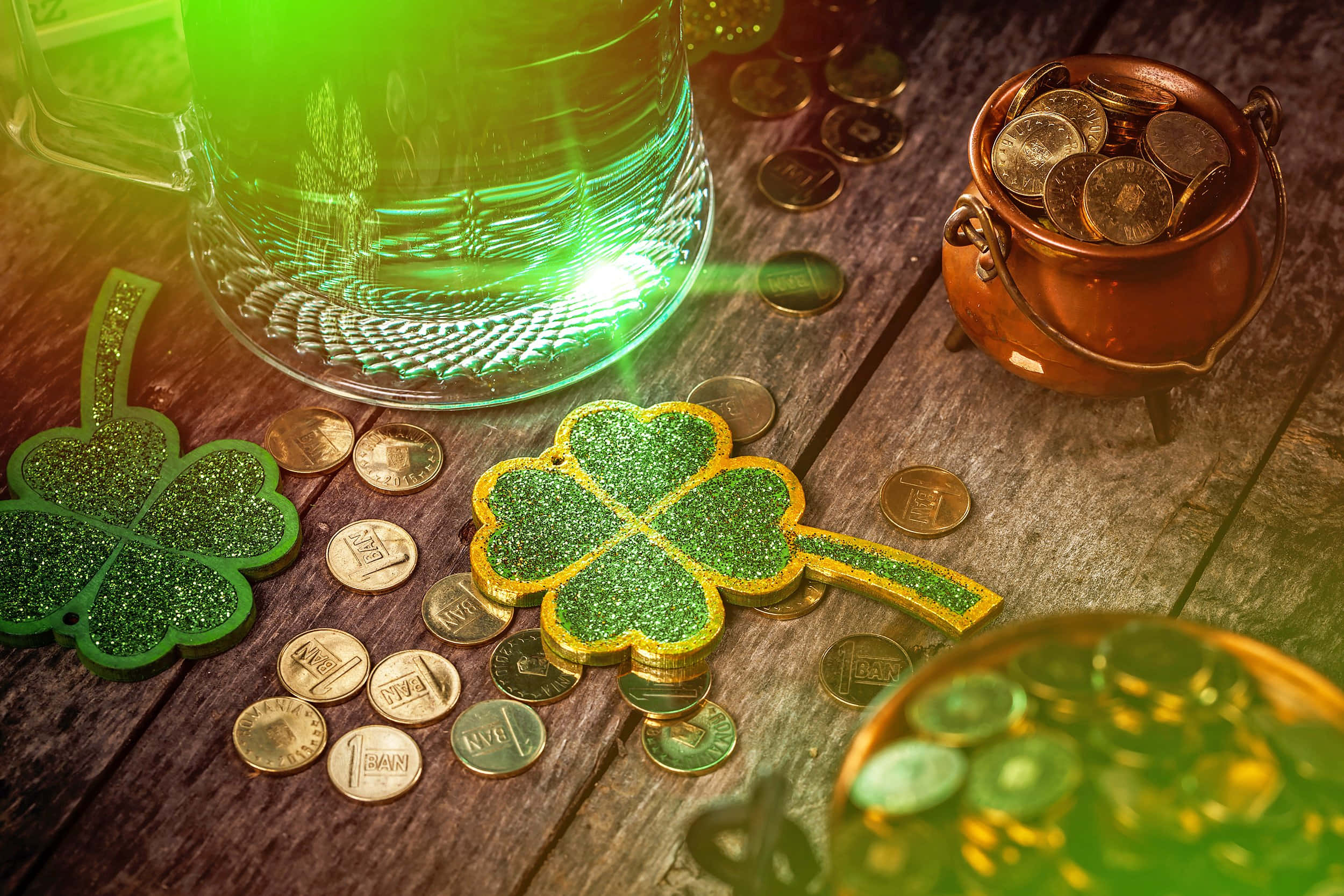 St Patrick's Day 桌布 壁紙 — 一張質樸的木桌上擺滿閃閃發光的三葉草、金幣和發光的綠色啤酒杯，營造出聖派翠克節的節日歡樂氣氛。