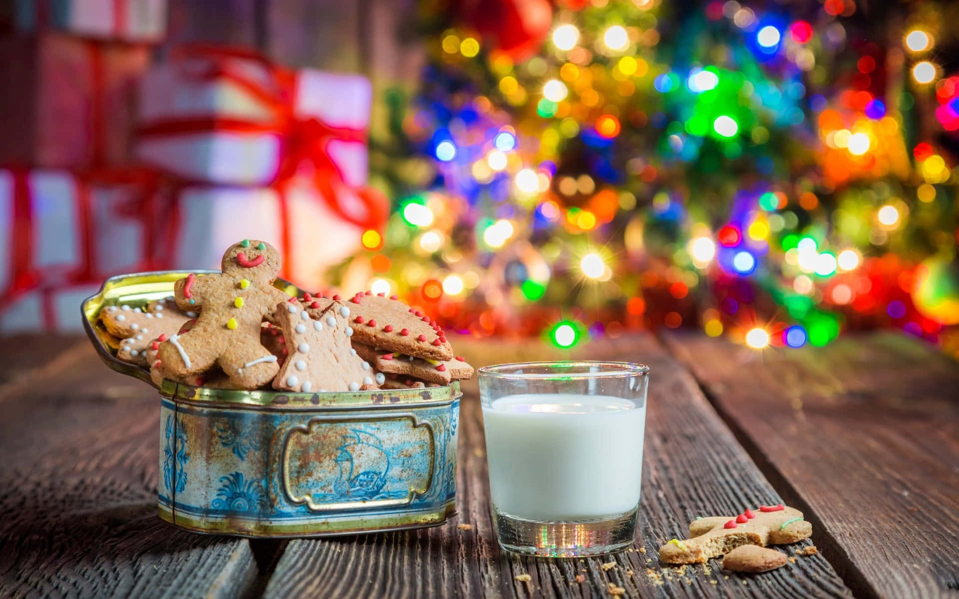 Winter Food 桌布 壁紙 — 一張質樸的木桌上放著一個復古罐子，裡面裝滿了薑餅餅乾，旁邊有一杯牛奶，背景是模糊的聖誕樹，掛滿了彩色燈飾。