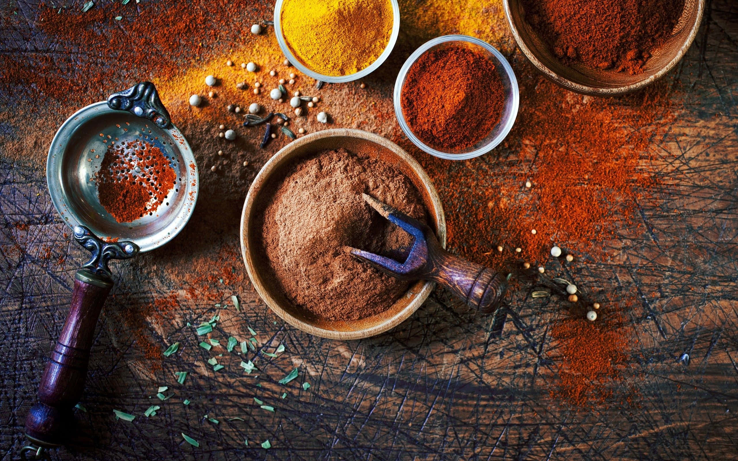 Spice 桌布 壁紙 — 一張質樸的木桌上散落著碗和篩子裡的鮮豔香料，展現出大地色調的紅、黃和綠色。