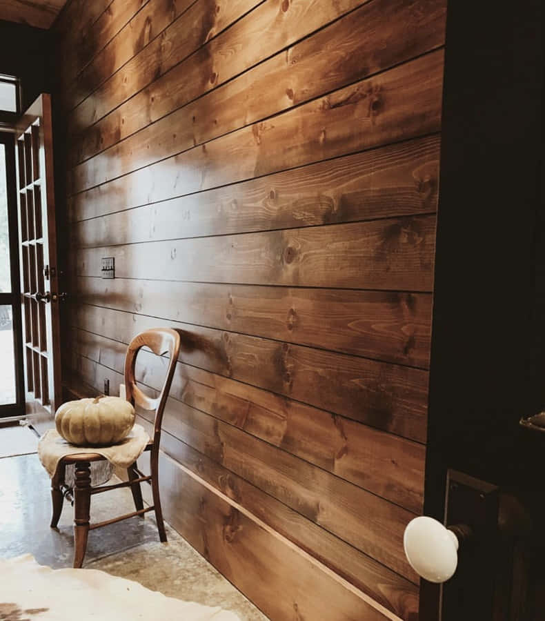 Shiplap 桌布 壁紙 — 一張質樸的木椅，上面放著一個南瓜，位於一個光線溫暖的房間裡，房間有豐富的木條牆壁和一扇玻璃門。