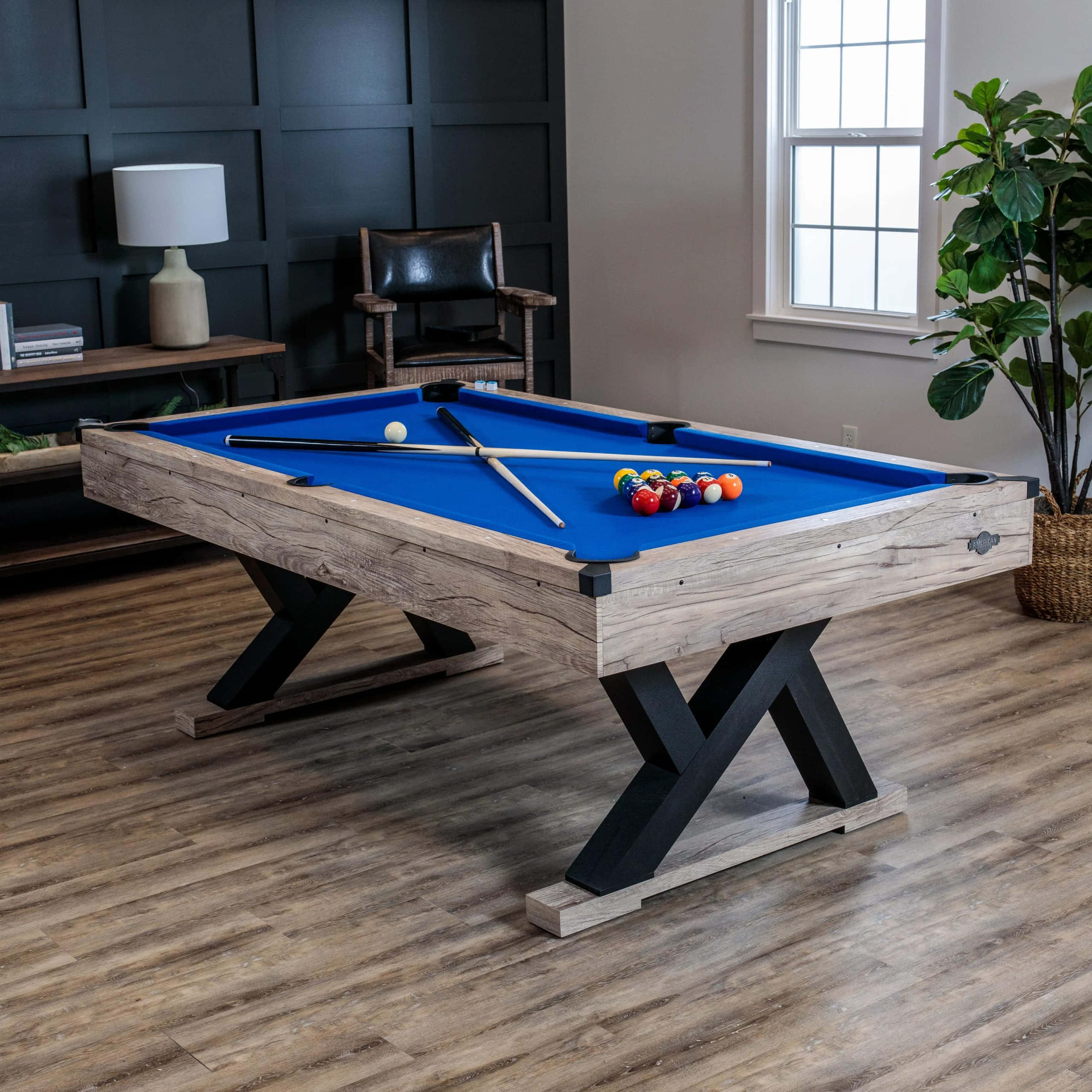 Pool Table 桌布 壁紙 — 一張質樸的木製撞球桌，配有藍色絨布和交叉的黑色桌腳，放置在現代風格的房間內，房間鋪有硬木地板並設有大窗戶。