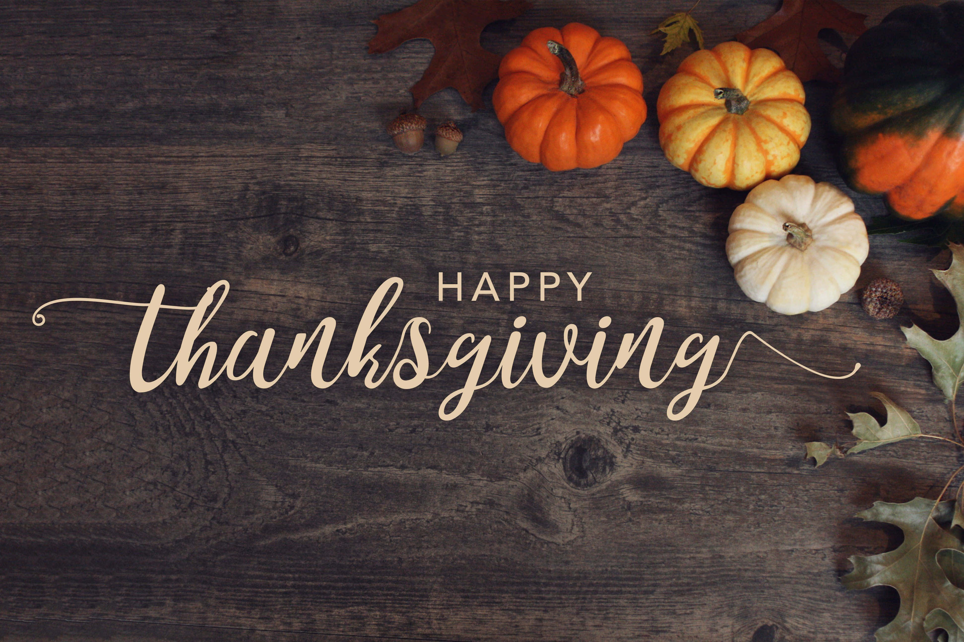 Happy Thanksgiving 桌布 壁紙 — 一張鄉村風木桌，裝飾著色彩繽紛的南瓜、橡果和樹葉，並以優雅的手寫字體寫著 happy thanksgiving。