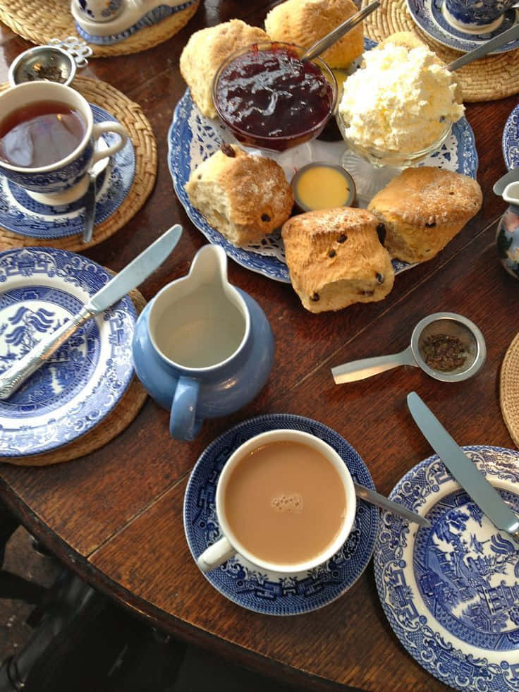 Teatime 桌布 壁紙 — 一張鄉村風格的木桌上擺放著藍白瓷器杯碟、司康、果醬、凝脂奶油和茶，營造出舒適的下午茶場景。