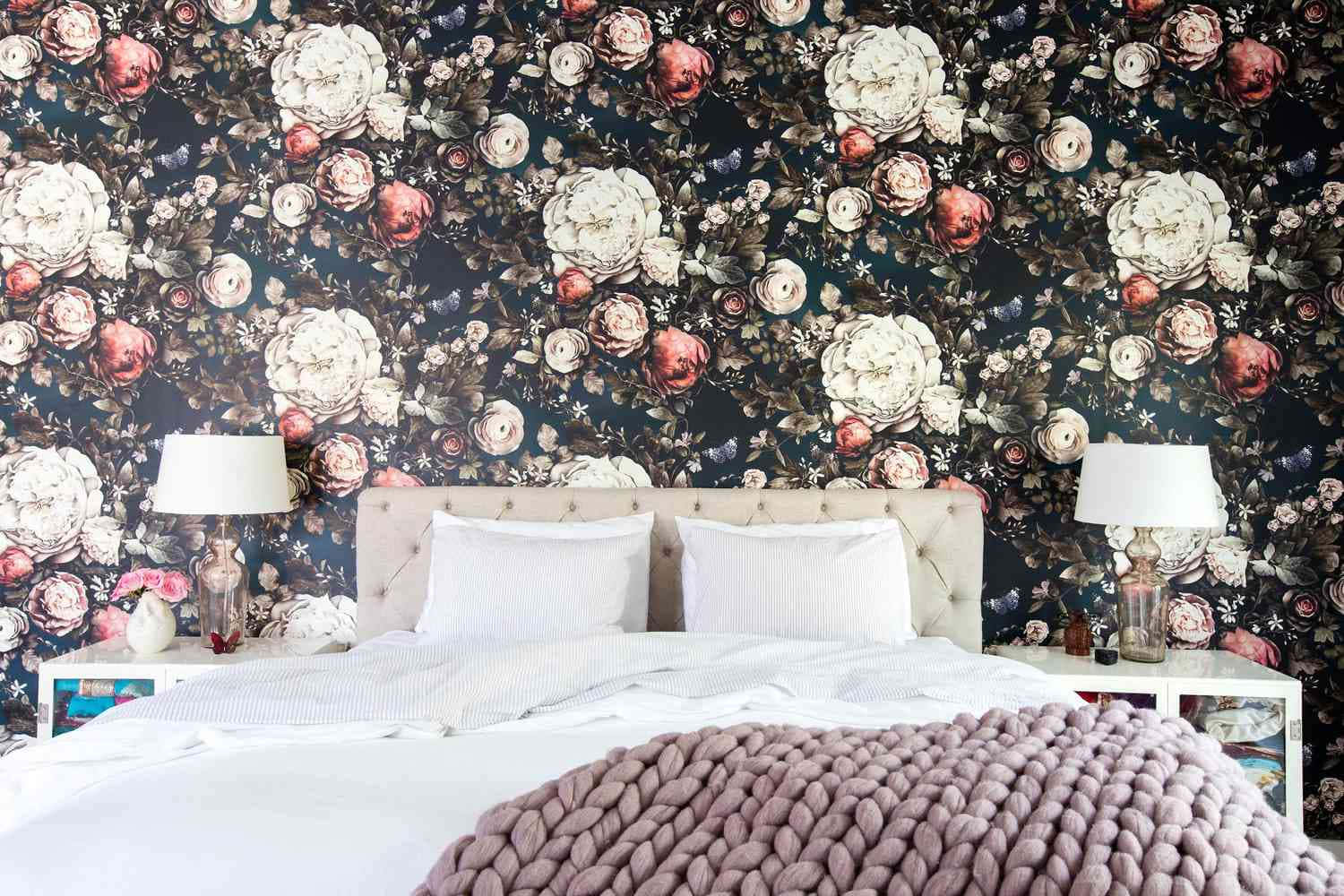 Bedroom 桌布 壁紙 — 一張鋪有白色床單和厚針織毯子的床，位於深色花卉壁紙下方，壁紙上有大朵的奶油色和紅色玫瑰。