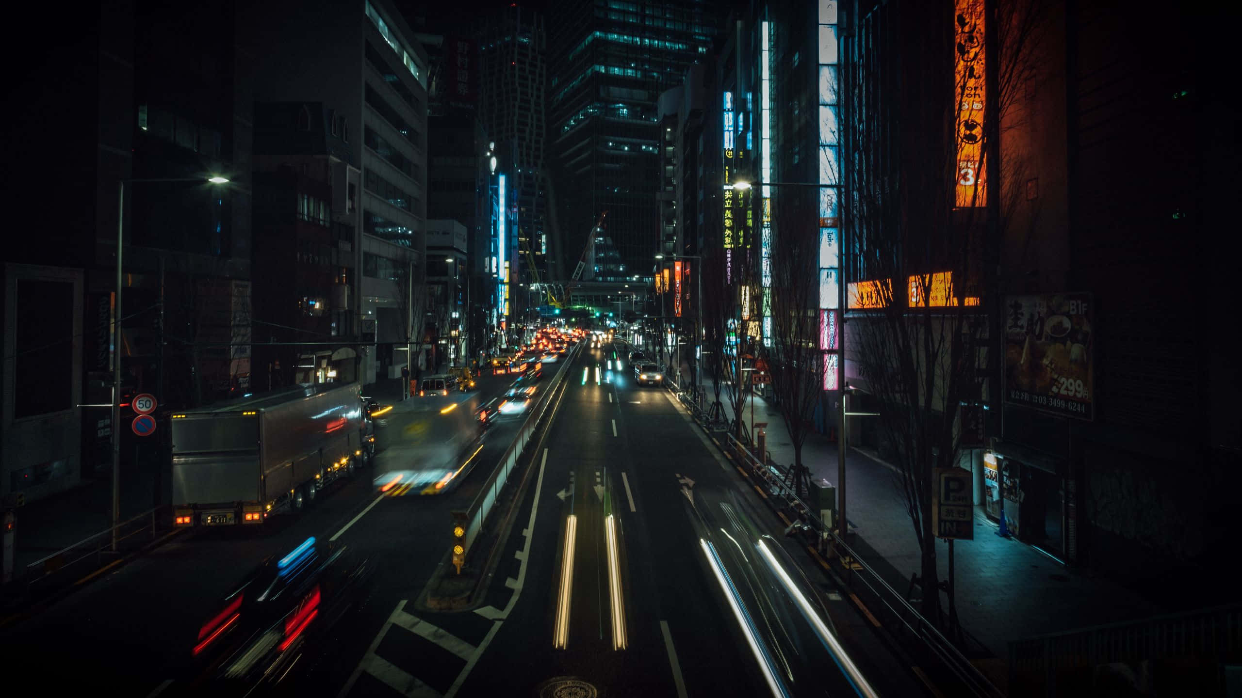 桌布 壁紙 — 一張長時間曝光照片，拍攝夜晚霓虹燈照亮的城市街道，車燈光線流過高樓大廈之間形成的光軌。