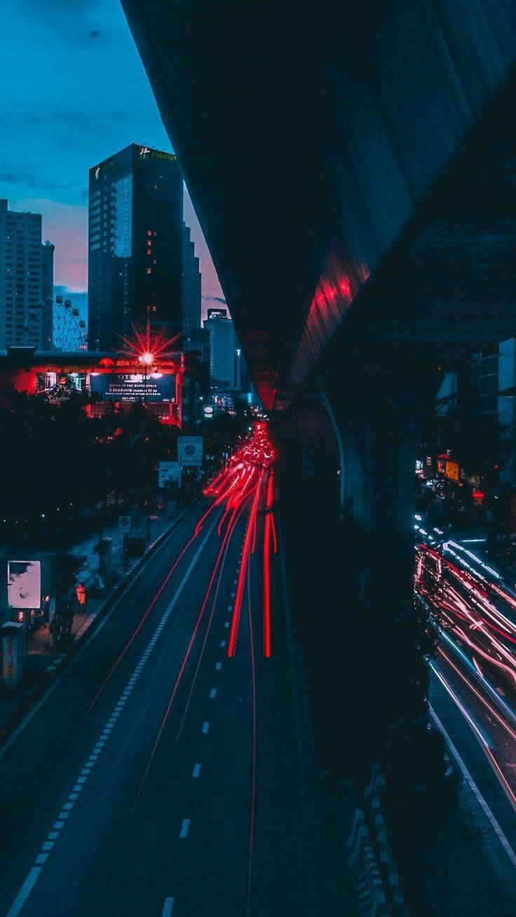 Trendy Aesthetic 桌布 壁紙 — 一張長時間曝光照片捕捉到在暮色城市景觀中，汽車在黑暗的天橋下飛馳時發出的紅色和白色光軌。