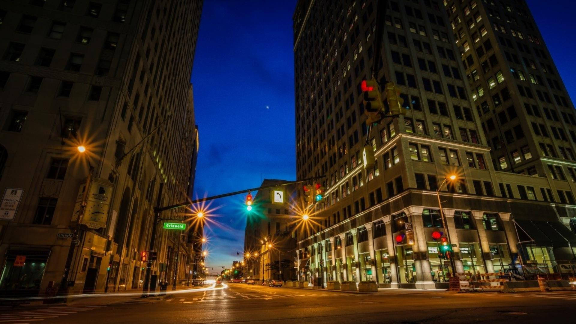 detroit 桌布 壁紙 — 一張長時間曝光的城市街道照片，在暮色中，高聳建築物之間有發光的交通燈和汽車燈光軌跡。