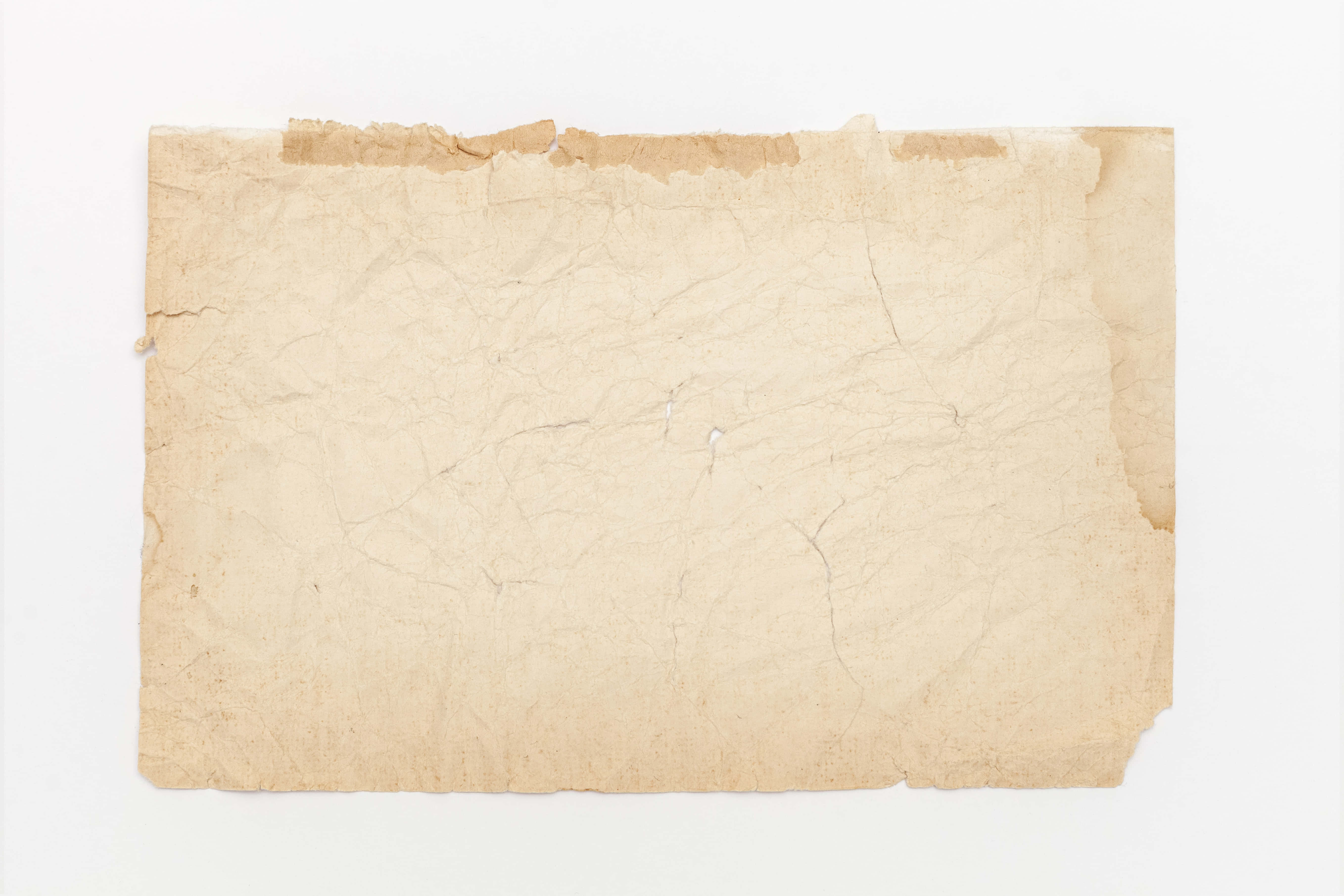 Old Paper 桌布 壁紙 — 一張陳舊的米色紙張，邊緣破損，帶有可見的摺痕，平放在純白色背景上。