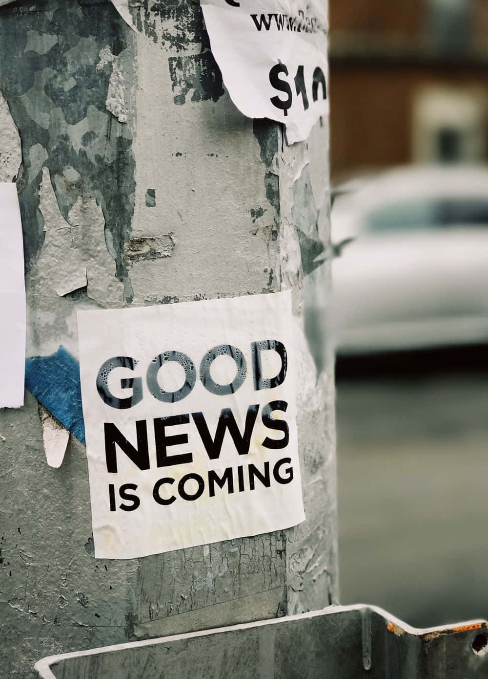 Gospel 桌布 壁紙 — 一張風化的貼紙宣告「GOOD NEWS IS COMING」，從佈滿灰塵的市區柱子上剝落，周圍是褪色的海報和城市衰敗。