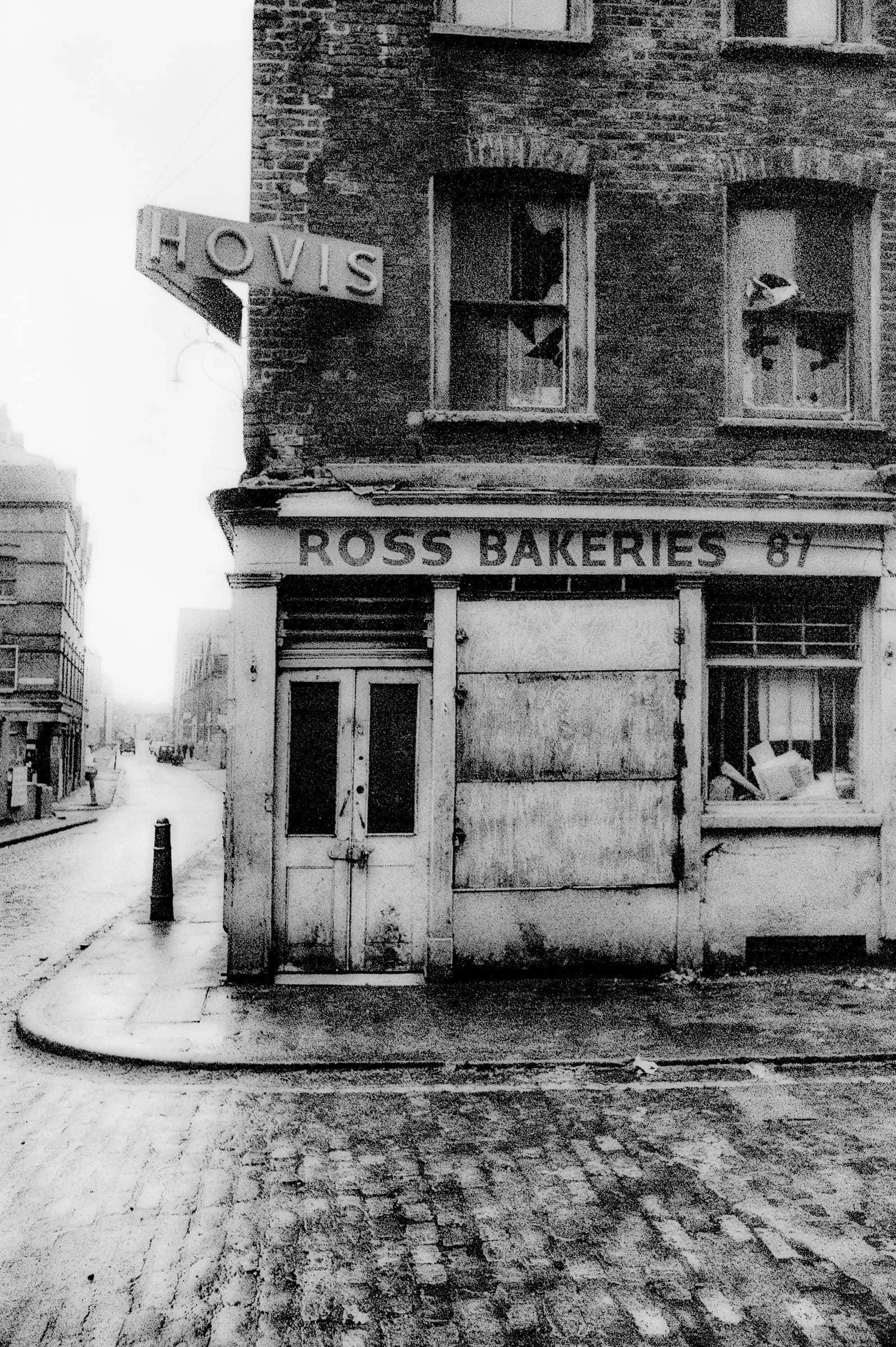復古 桌布 壁紙 — 一張飽經風霜的黑白照片，顯示羅斯烘焙坊（Ross Bakeries）用木板封住的店面，窗戶破損，褪色的Hovis招牌，位於鵝卵石街道上。