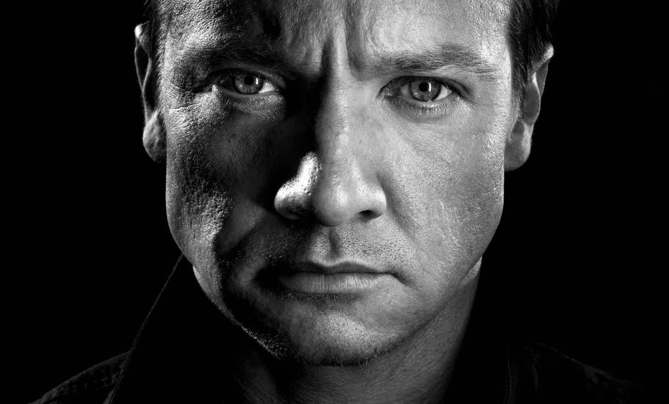 Jeremy Renner 桌布 壁紙 — 一張高對比度的黑白特寫肖像，拍攝對象是一名眼神銳利、表情嚴肅的男子，背景為深色。