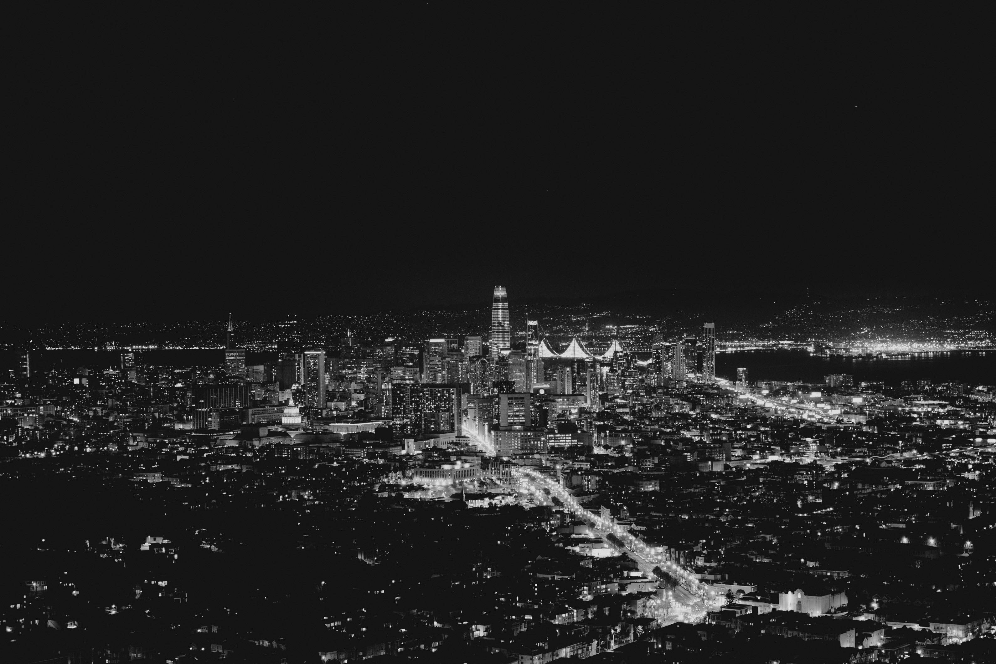 Sans 桌布 壁紙 — 一張高角度黑白夜景照片，展現了廣闊的城市景觀，燈光閃爍照亮摩天大樓和街道。