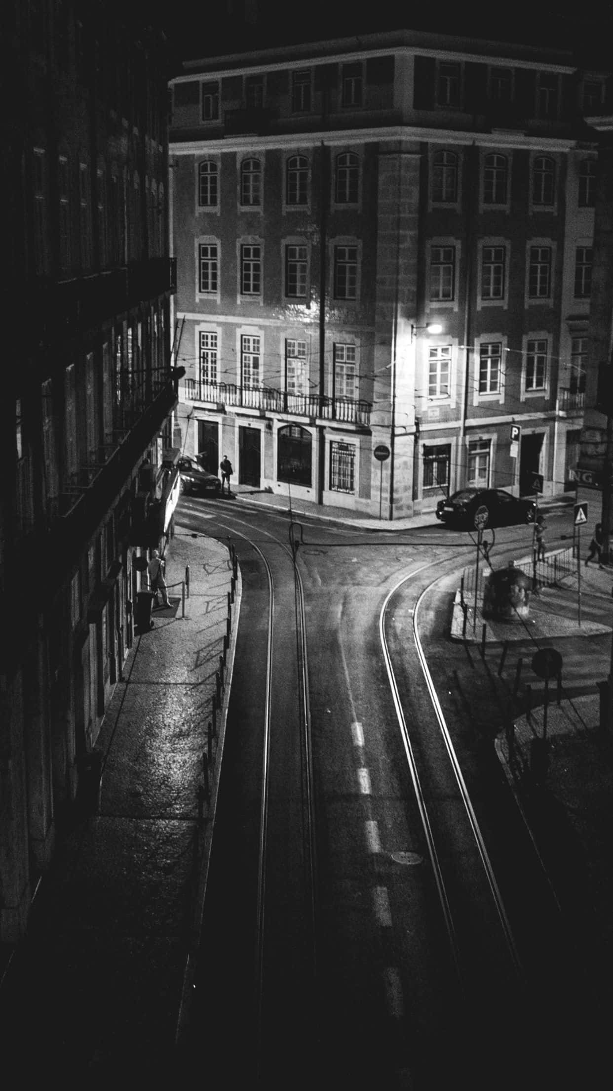 Black And White Street 桌布 壁紙 — 一張高角度黑白夜景照片，拍攝濕漉漉的城市街道，電車軌道在歷史建築之間蜿蜒。