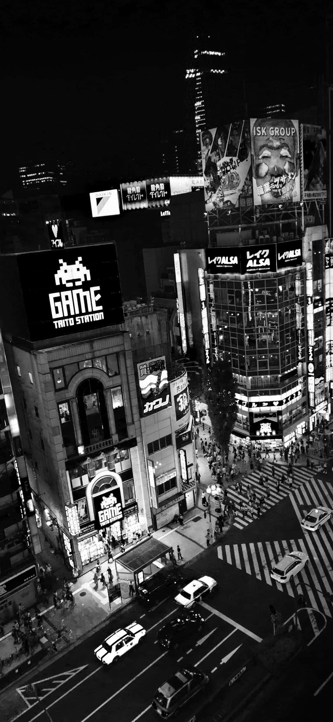 Black And White iPhone 桌布 壁紙 — 一張高角度黑白照片，拍攝了夜晚繁忙的東京街道，有發光的廣告牌和過馬路的行人。