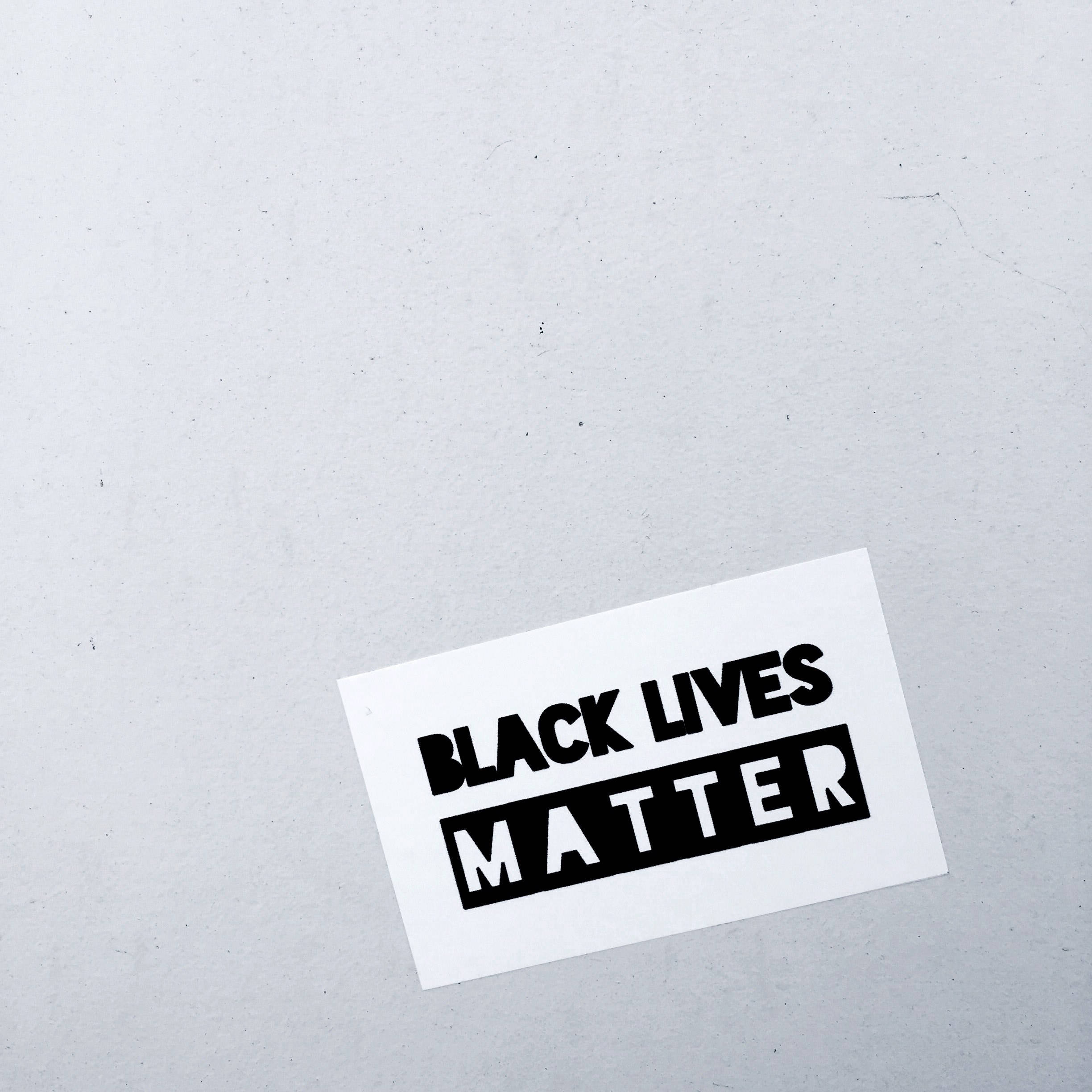 藝術 桌布 壁紙 — 一張鮮明的黑白「BLACK LIVES MATTER」貼紙傾斜地放在有紋理的灰色表面上。