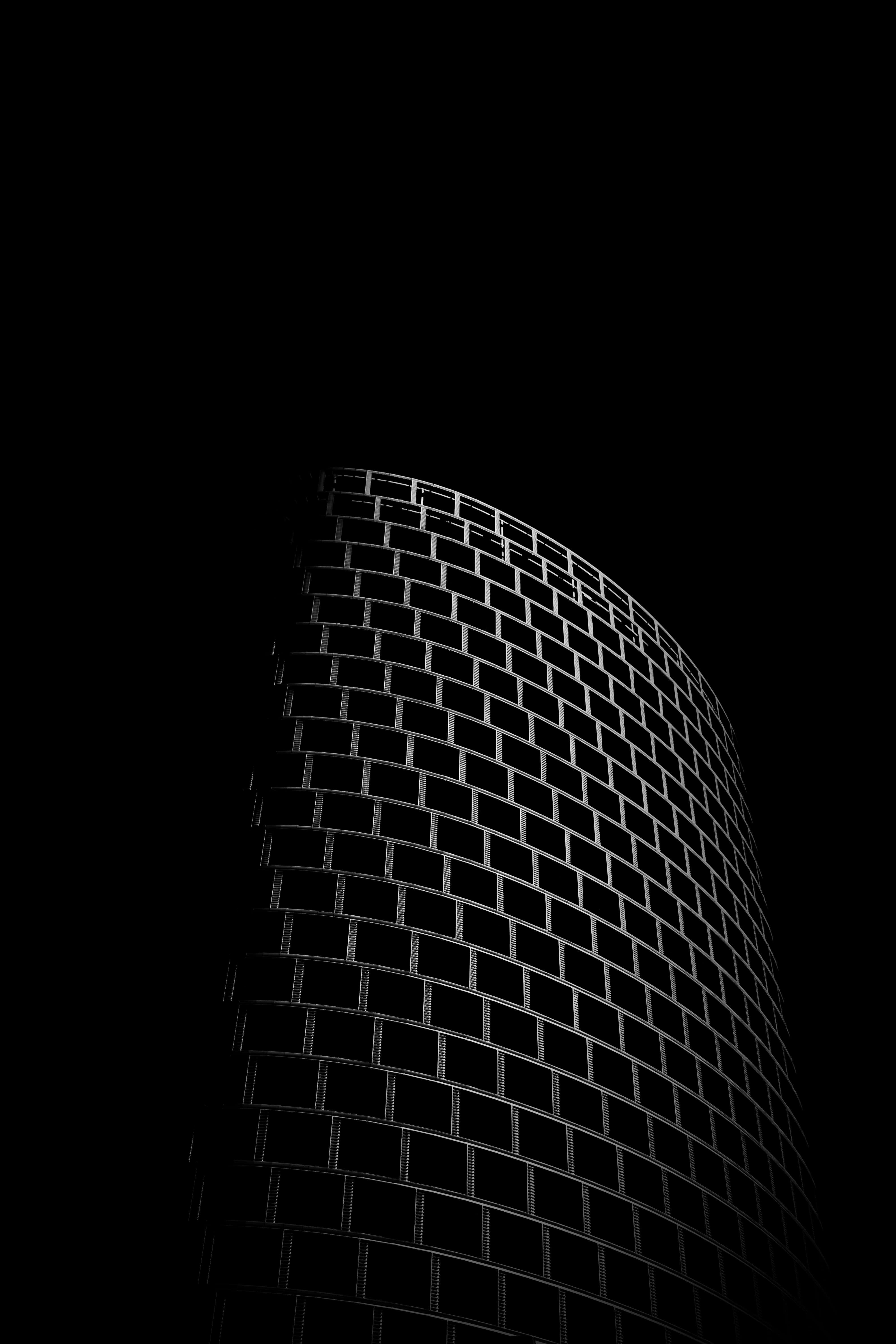 抽象 桌布 壁紙 — 一張鮮明的黑白低角度照片，拍攝彎曲玻璃摩天大樓的剪影，背景是漆黑的天空。