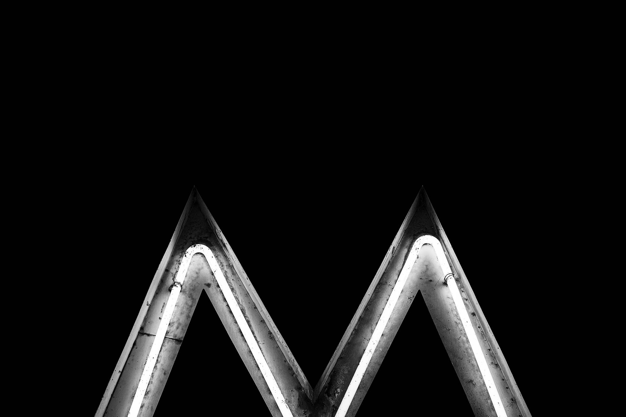 字母M 桌布 壁紙 — 一張鮮明的黑白照片，展示一個發光的霓虹字母M，背景為漆黑一片。