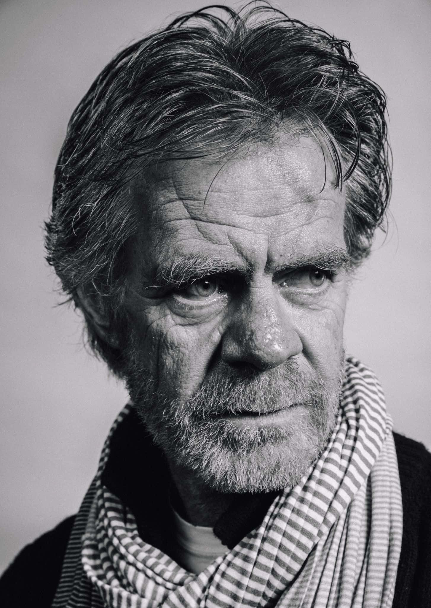william h. macy 桌布 壁紙 — 一張鮮明黑白肖像，捕捉一位歷經風霜、眼神銳利、圍著條紋圍巾的男子，直視觀者。
