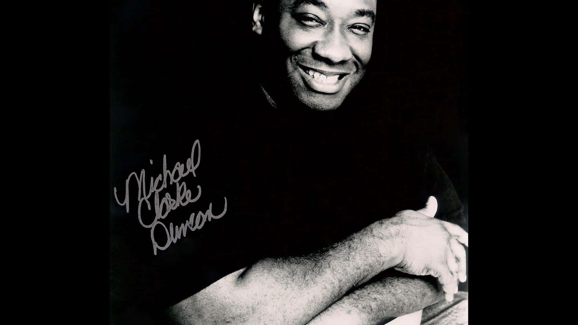 Michael Clarke Duncan 桌布 壁紙 — 一張麥可·克拉克·鄧肯的黑白肖像，他雙手合十，在深色背景下溫暖地微笑。