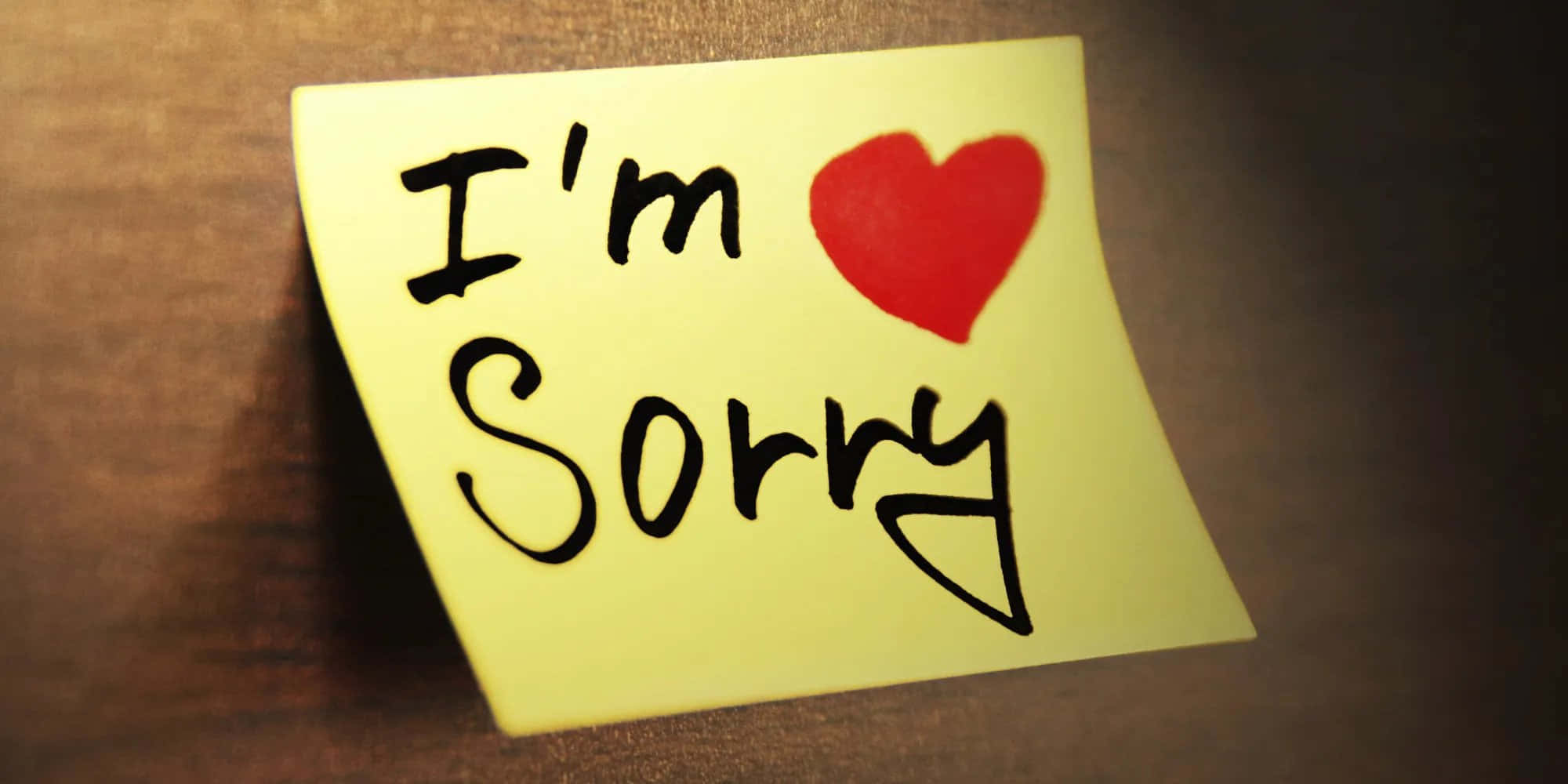Handwriting 桌布 壁紙 — 一張黃色便利貼，上面有手寫的「I'm Sorry」和一個紅色愛心，放在木質表面上。