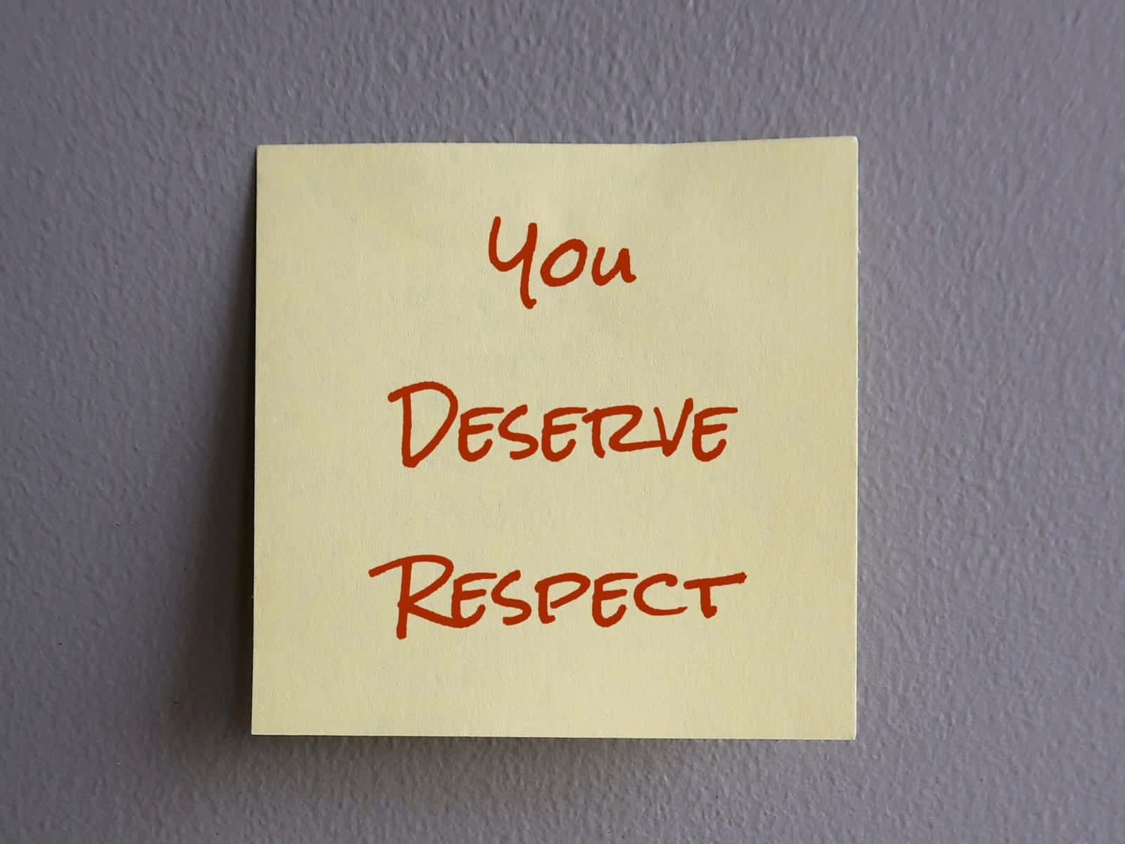 Respect 桌布 壁紙 — 一張黃色便利貼，上面有紅色手寫文字「你值得尊重」，貼在紋理灰牆上。