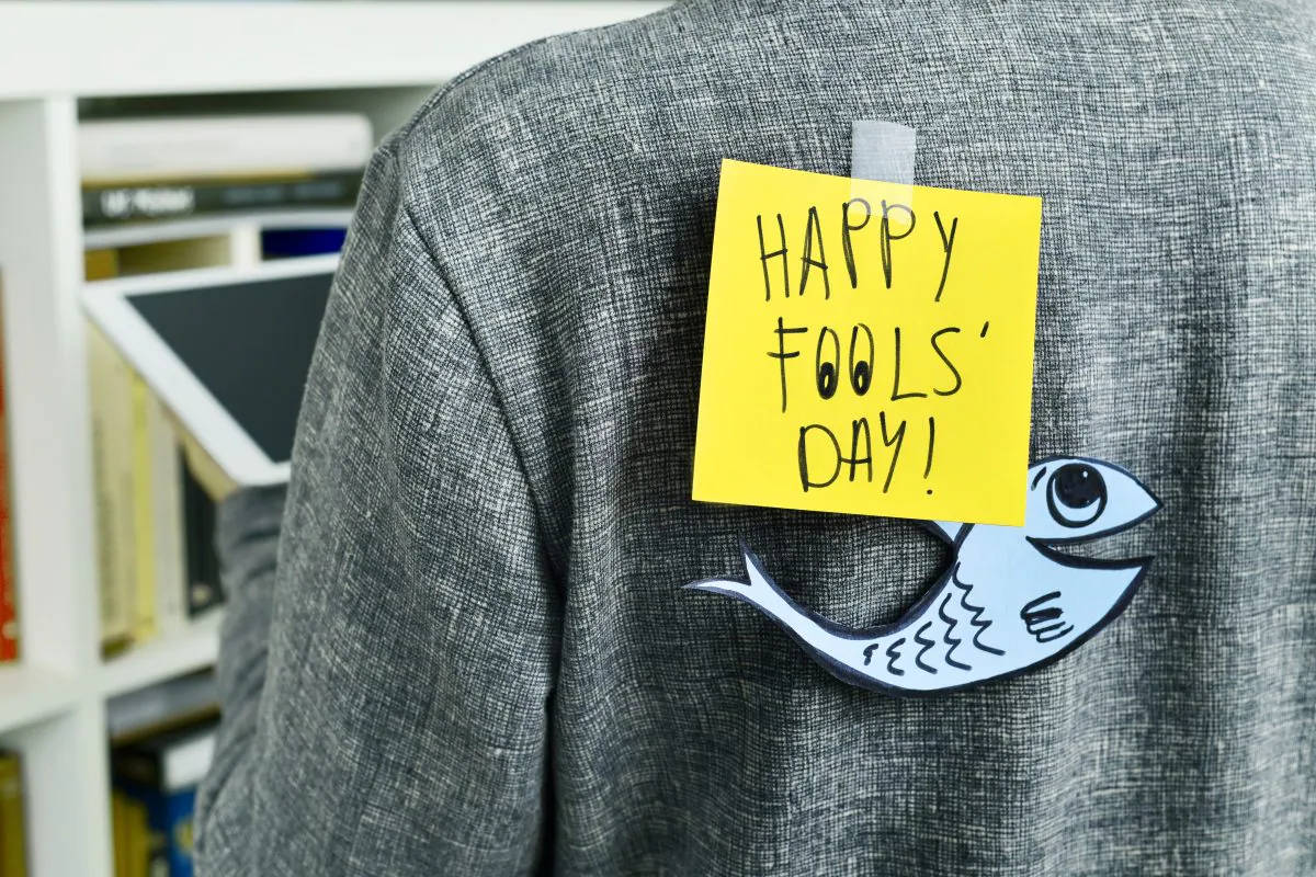 Fools 桌布 壁紙 — 一張黃色便利貼寫著「HAPPY FOOLS' DAY!」，貼在灰色外套上，下方有一個紙魚剪影。