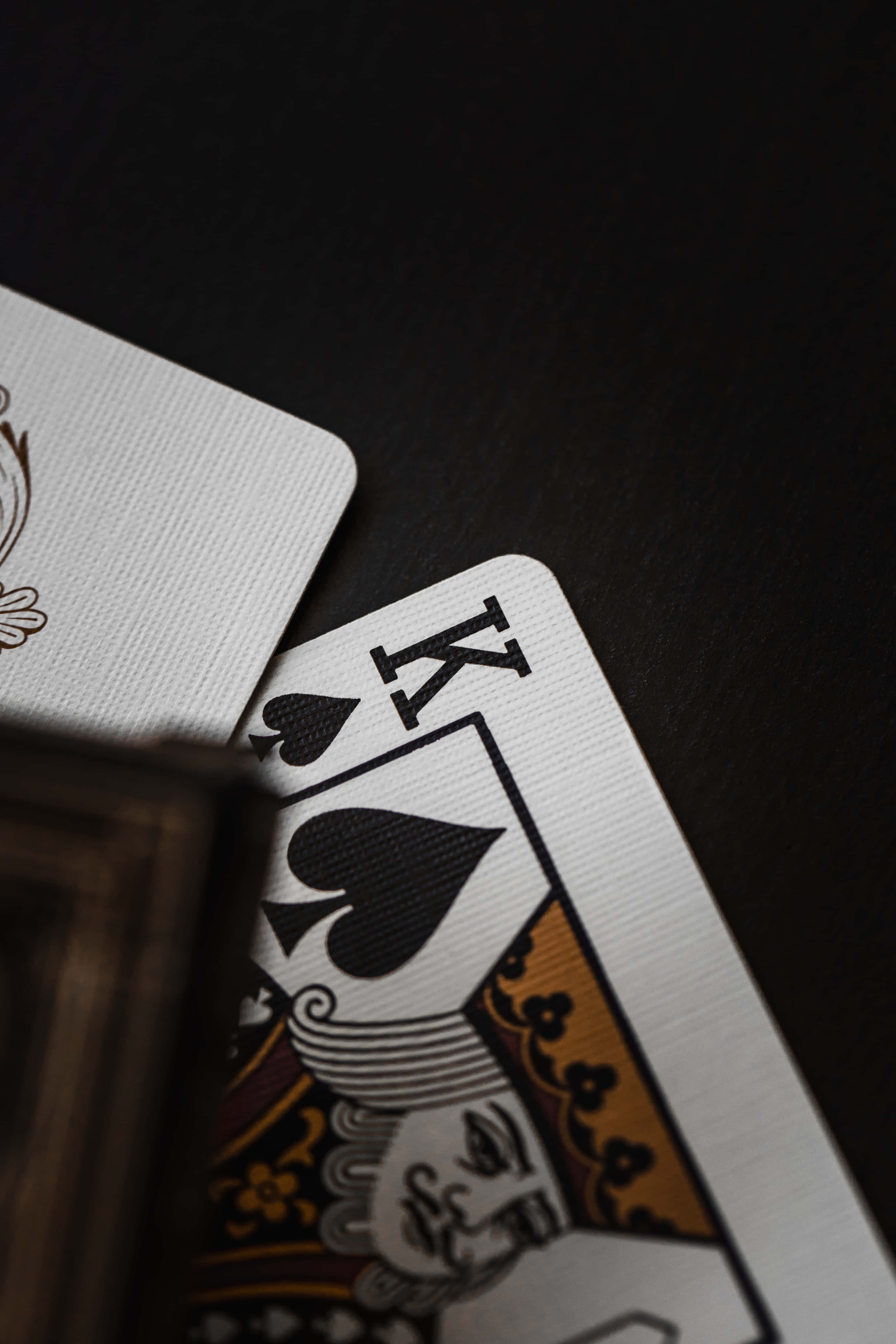 Playing Cards 桌布 壁紙 — 一張黑桃K撲克牌局部重疊在另一張牌上，置於深色紋理表面的特寫。