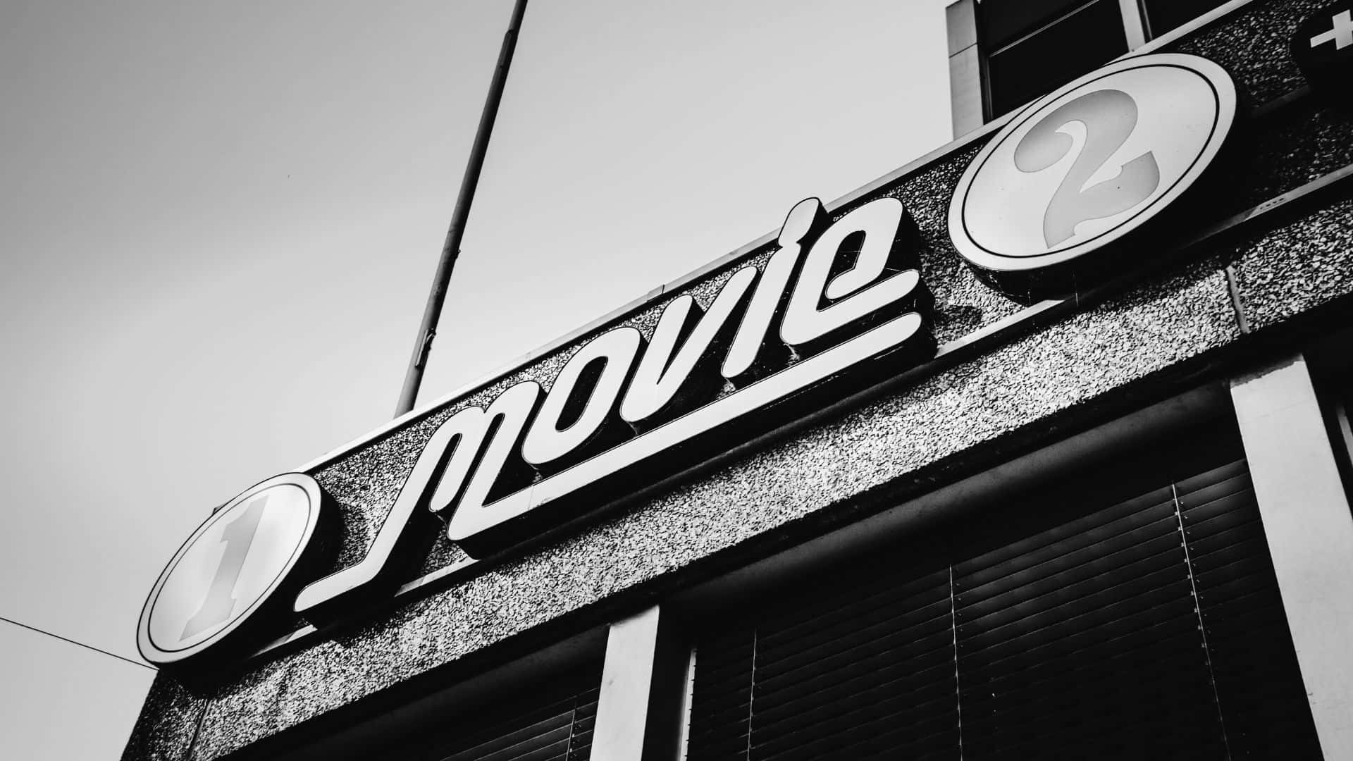 Black And White Movie 桌布 壁紙 — 一張黑白低角度拍攝的復古電影院招牌照片，帶有粗體字和圓形數字顯示。