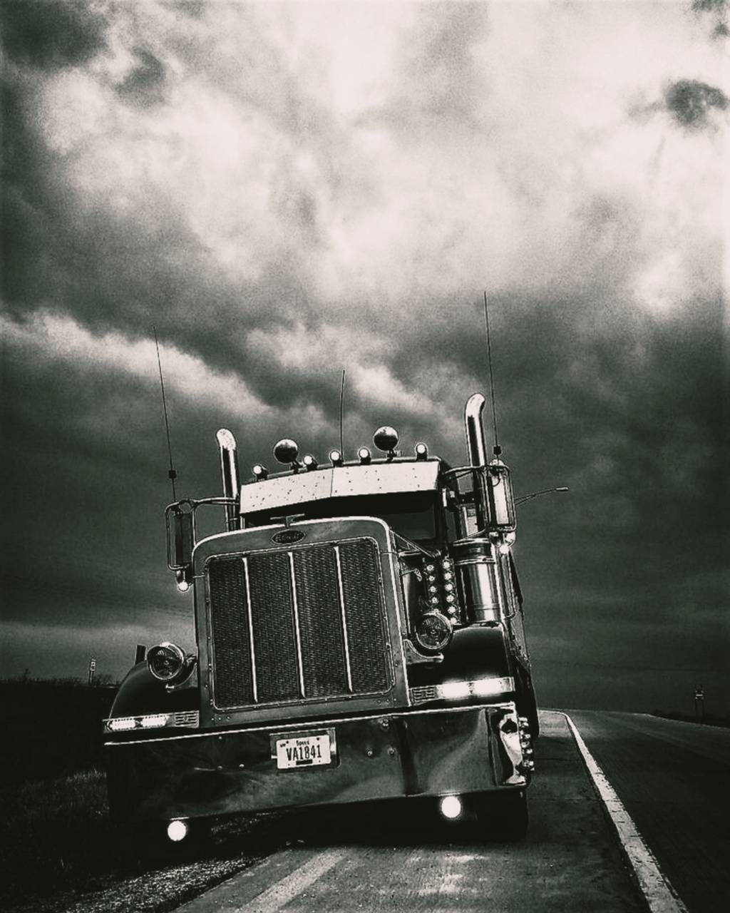 Peterbilt 桌布 壁紙 — 一張黑白低角度拍攝的經典半掛卡車在孤獨的高速公路上駛近，背景是戲劇性的暴風雨天空。