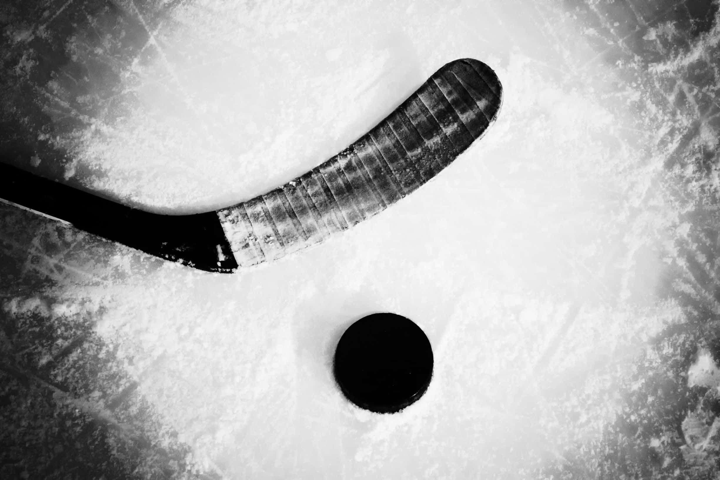 hockey 桌布 壁紙 — 一張黑白俯拍照片，展示磨損的曲棍球棍和冰球在紋理冰面上。