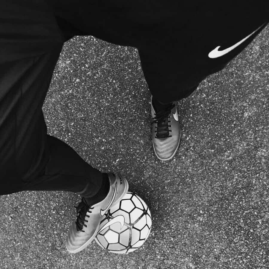 Nike 桌布 壁紙 — 一張黑白俯拍照片，顯示一名身穿黑色Nike裝備的人正在粗糙的瀝青表面上控制足球。