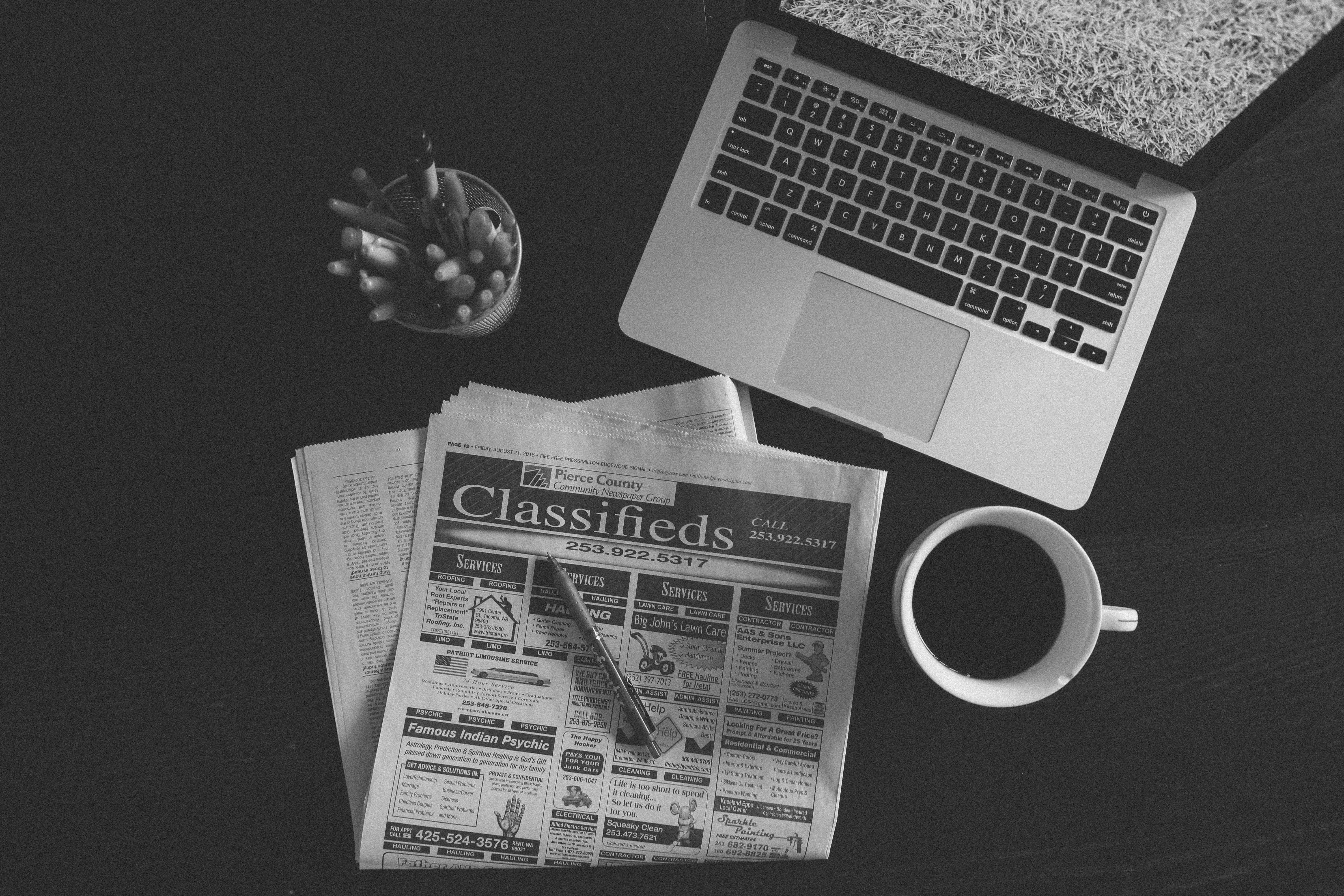 Newspaper 桌布 壁紙 — 一張黑白俯拍照片，顯示筆記型電腦、報紙、鉛筆和咖啡杯排列在深色桌子上。