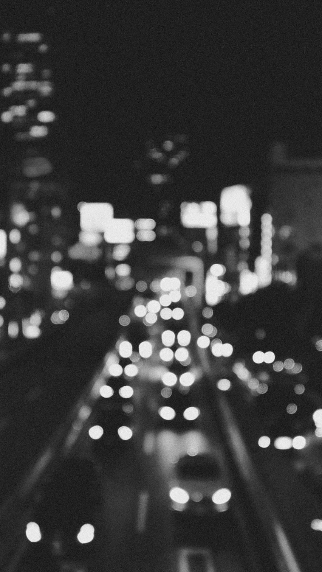 Black And White iPhone 桌布 壁紙 — 一張黑白散景拍攝的城市夜間交通照片，帶有發光的車頭燈和模糊的摩天大樓。