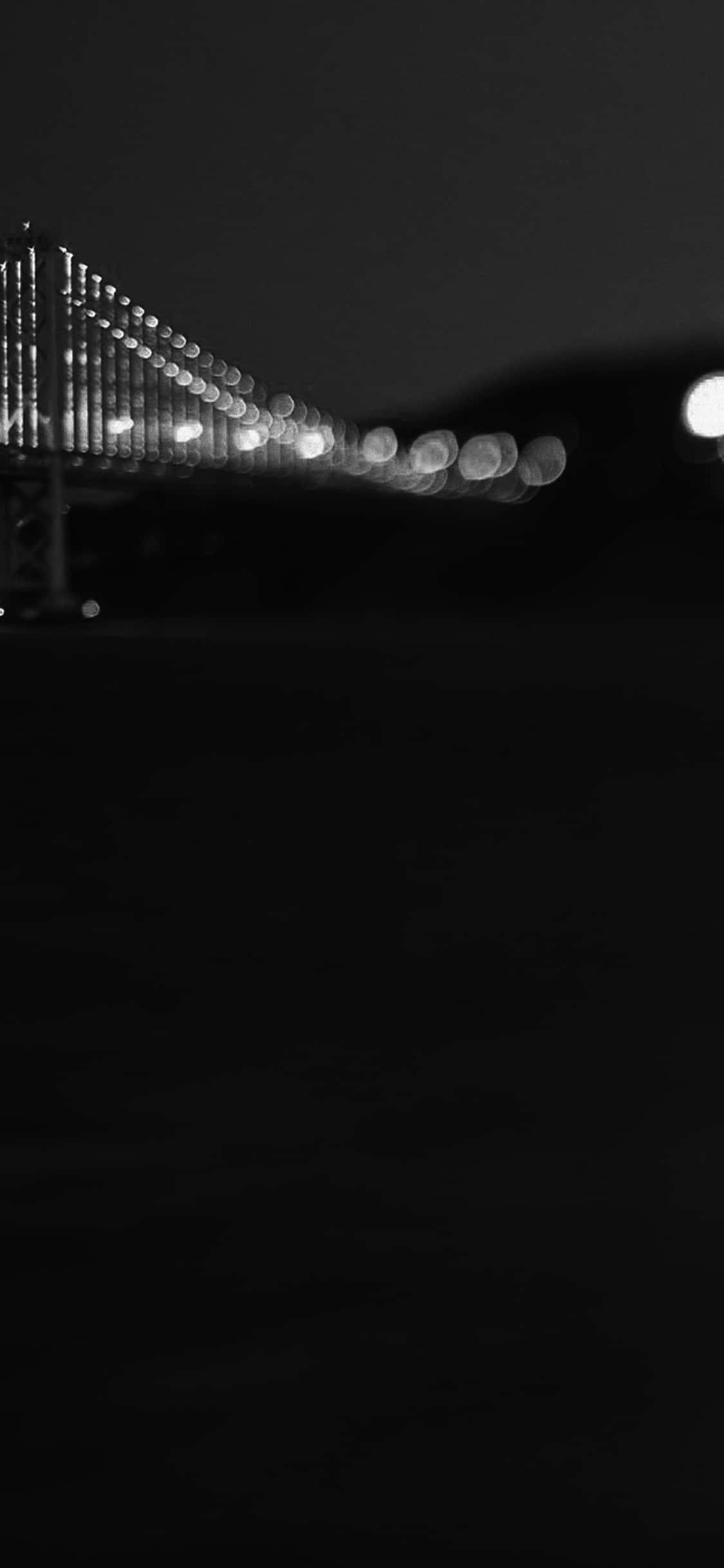 iPhone X California 桌布 壁紙 — 一張黑白散景照片，拍攝夜晚中燈火通明的吊橋，發光球體在黑暗天空的襯托下。