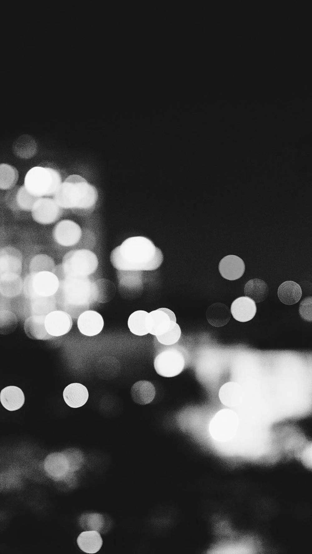 Bokeh 桌布 壁紙 — 一張黑白散景照片，模糊的城市燈光在黑暗的夜空中柔和發光。