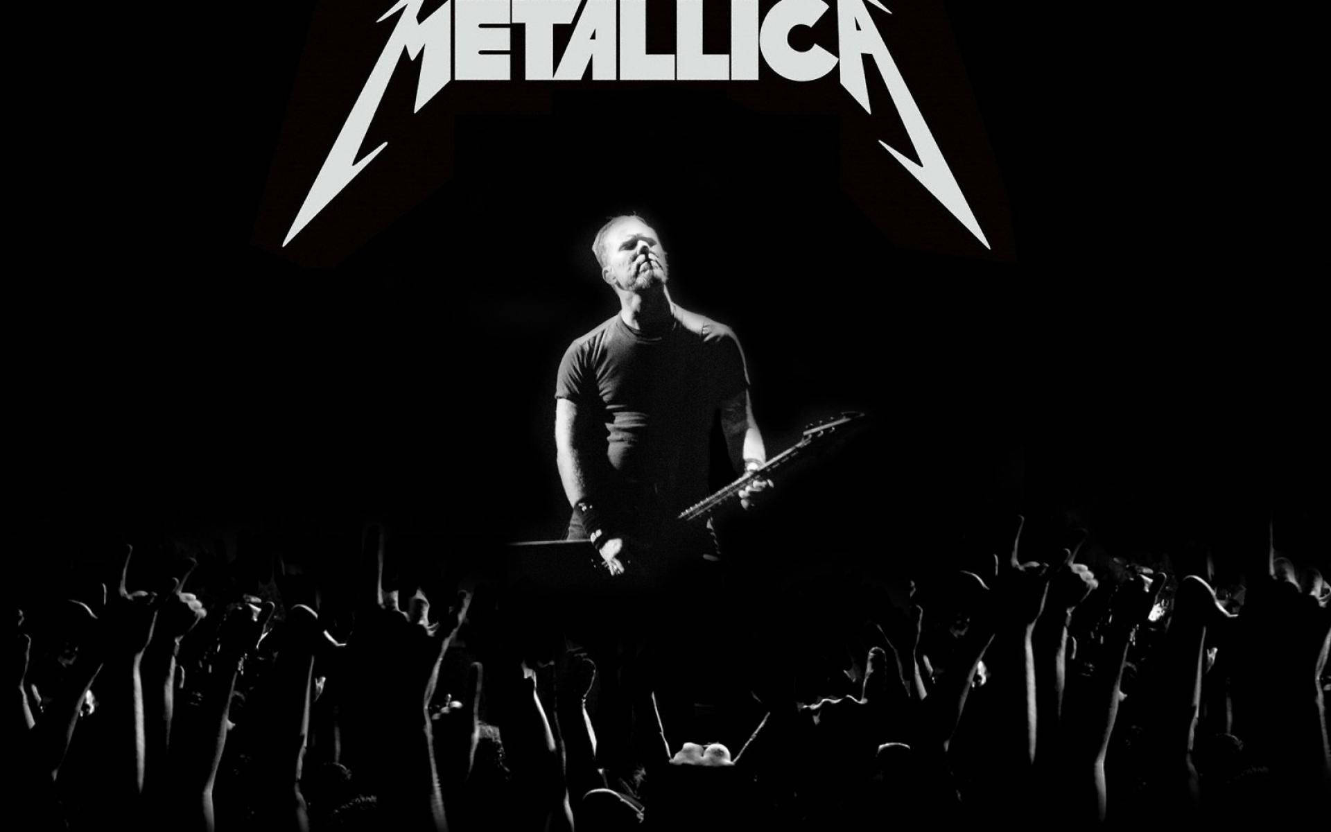金屬製品樂團 桌布 壁紙 — 一張黑白演唱會照片，Metallica 主唱在舞台燈光下拿著吉他，下方有舉起手的人群。