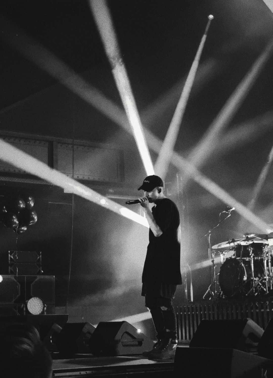 Nf Rapper 桌布 壁紙 — 一張黑白演唱會照片中，音樂家在戲劇性的光束下於舞台上表演。