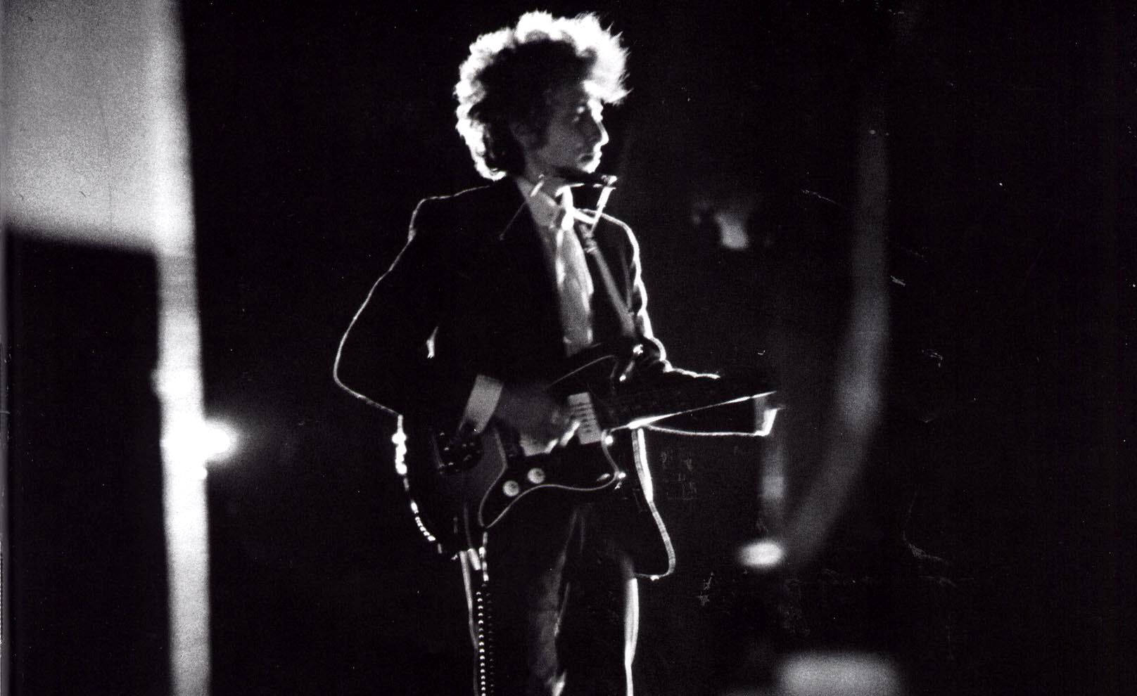 黑白 桌布 壁紙 — 一張黑白照片，Bob Dylan 在舞台上於戲劇性的聚光燈下彈奏電吉他。
