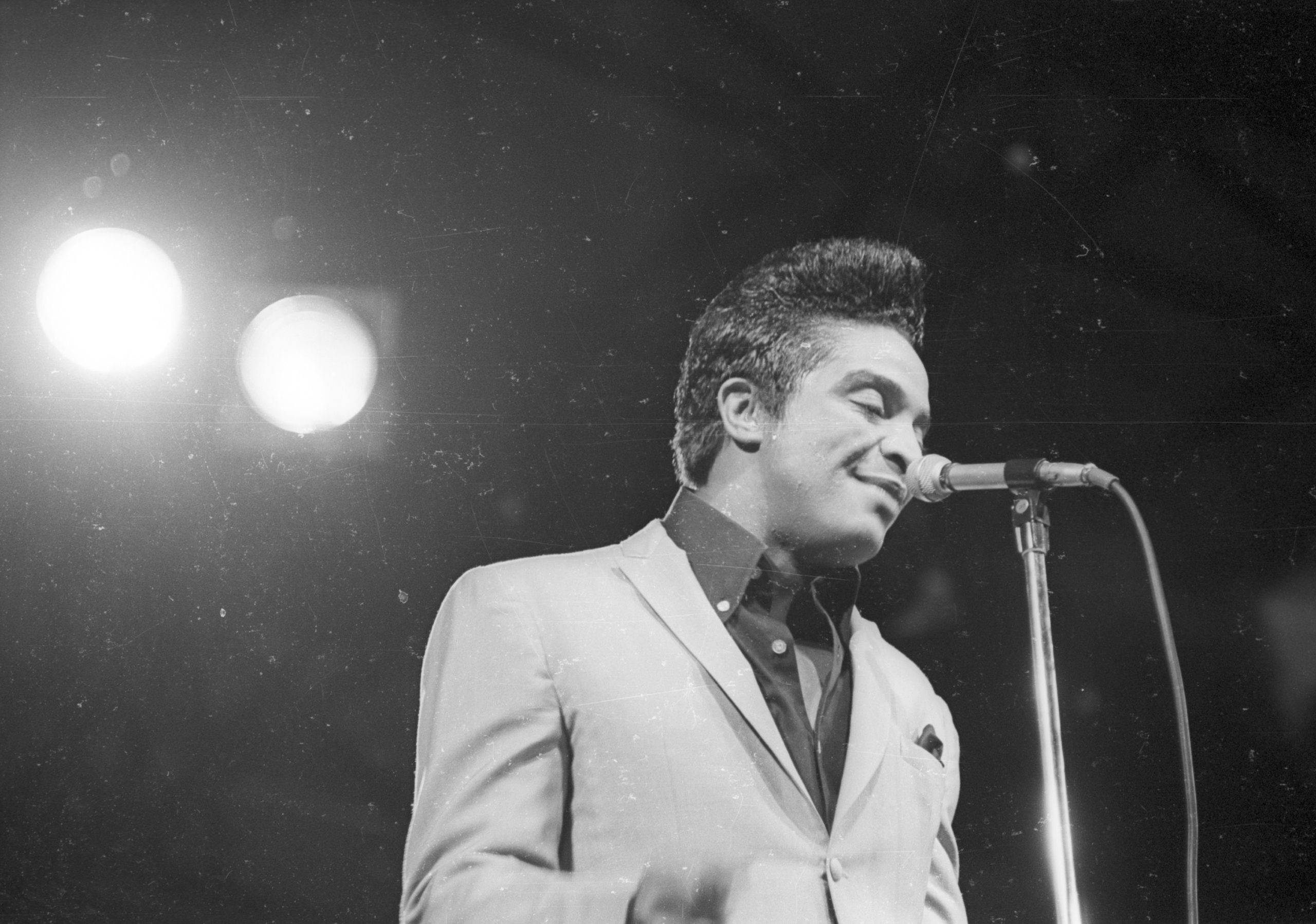 Singer 桌布 壁紙 — 一張黑白照片，一位身穿西裝、面帶微笑的男歌手在明亮的聚光燈下於舞台上表演。